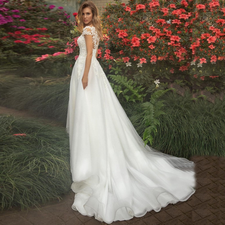 Elegant Wedding Dresses Vertigo De Novia featuring short sleeves, scoop neck illusion, and flower appliqué details in tulle fabric.