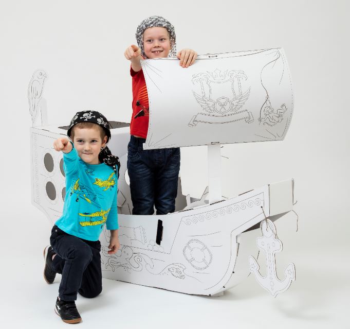A large DIY cardboard pirate ship for kids, featuring a steering wheel, anchor, and cabin, ready for imaginative play.