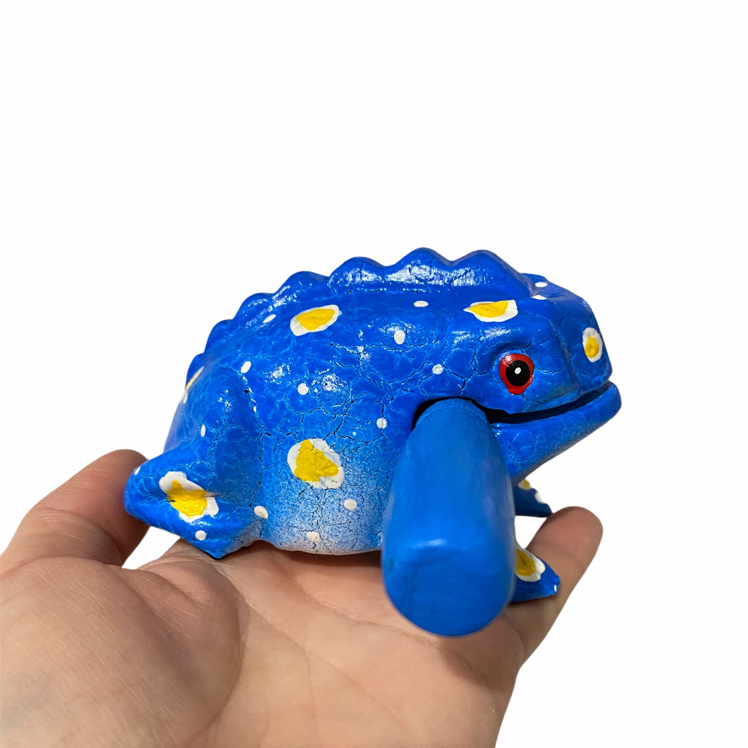A beautifully crafted Medium Painted Winter Frog musical percussion instrument, showcasing vibrant colors and intricate details, with a small wooden mallet resting in its mouth.