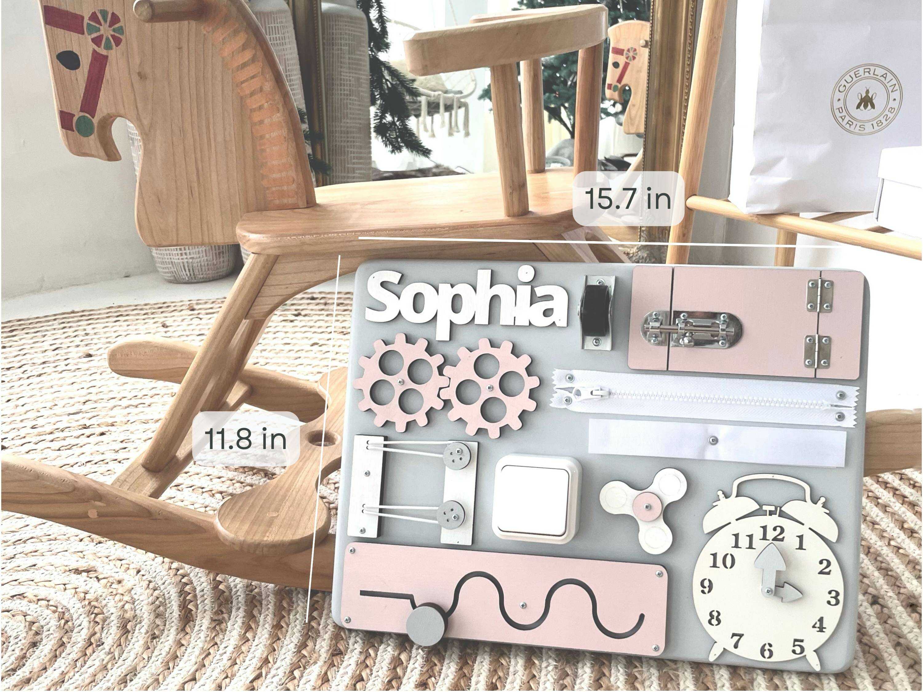 Mini Busy Board in pastel pink featuring various interactive elements for toddlers to enhance motor skills and creativity.