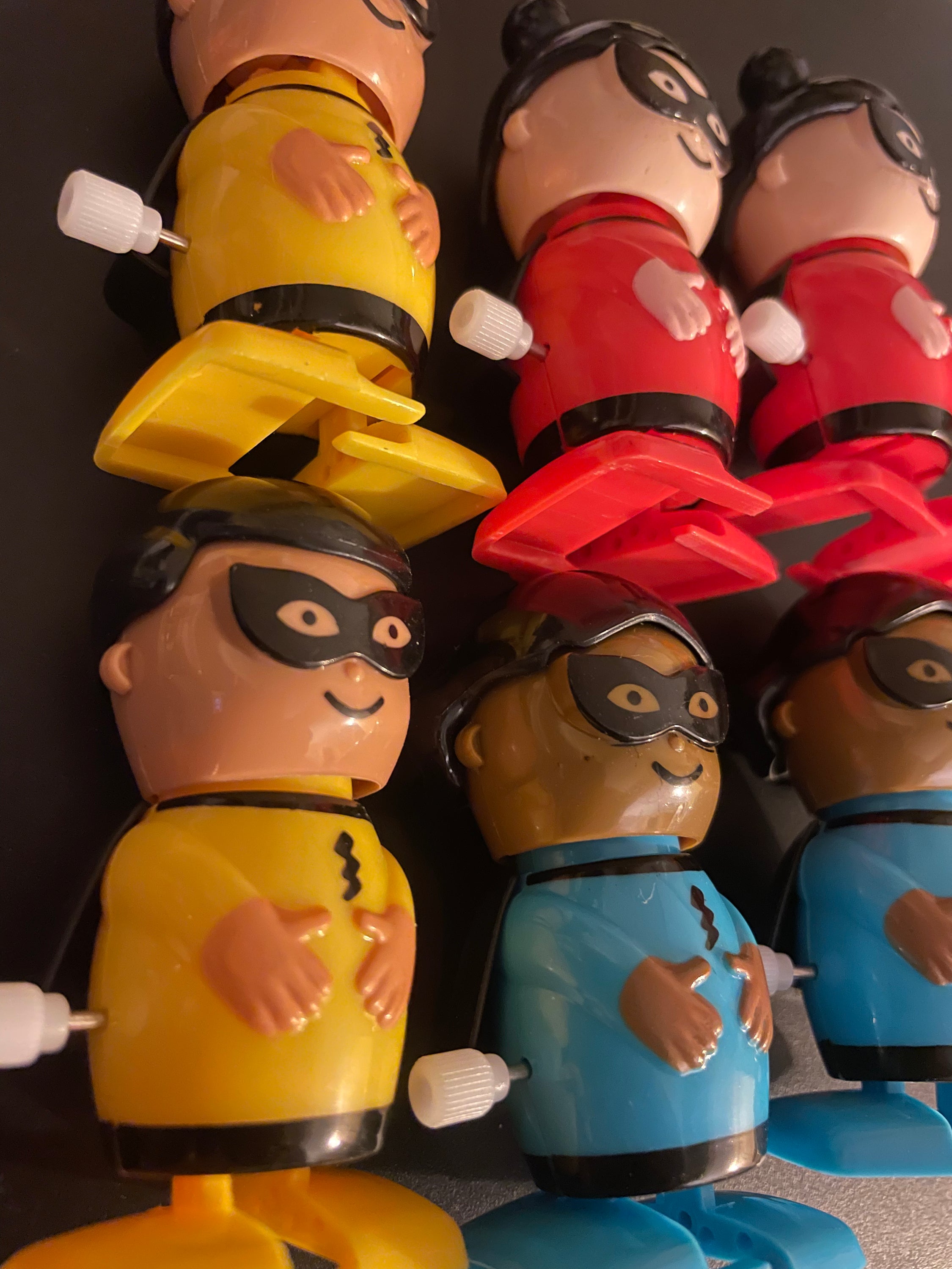 A colorful assortment of six wind-up superhero toys in yellow, red, and blue, showcasing their vibrant designs.