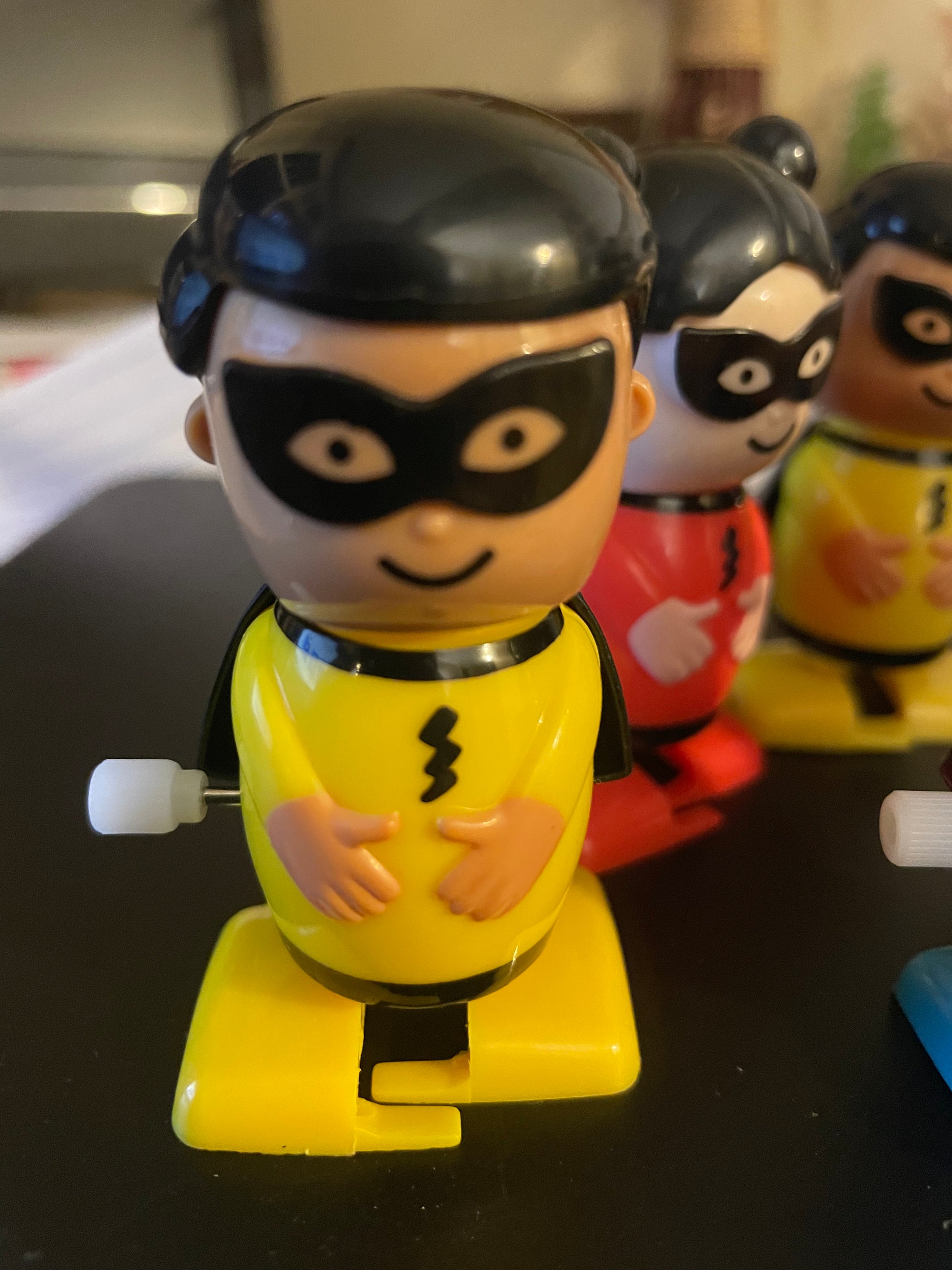 A colorful assortment of six wind-up superhero toys in yellow, red, and blue, showcasing their vibrant designs.