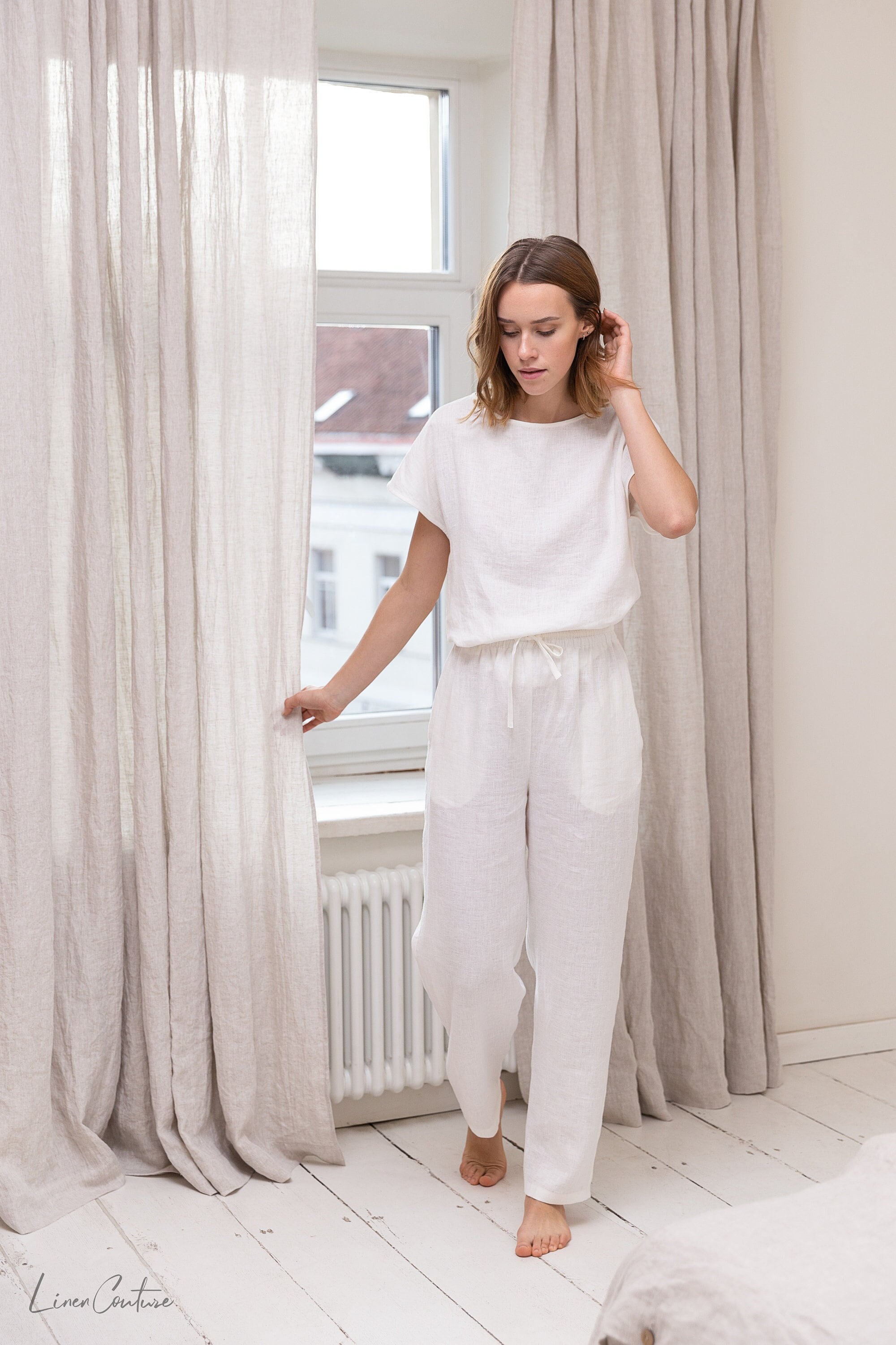 Elegant white linen pajama set featuring a boat neckline, short sleeves, and long pants with an adjustable waistband, perfect for lounging.
