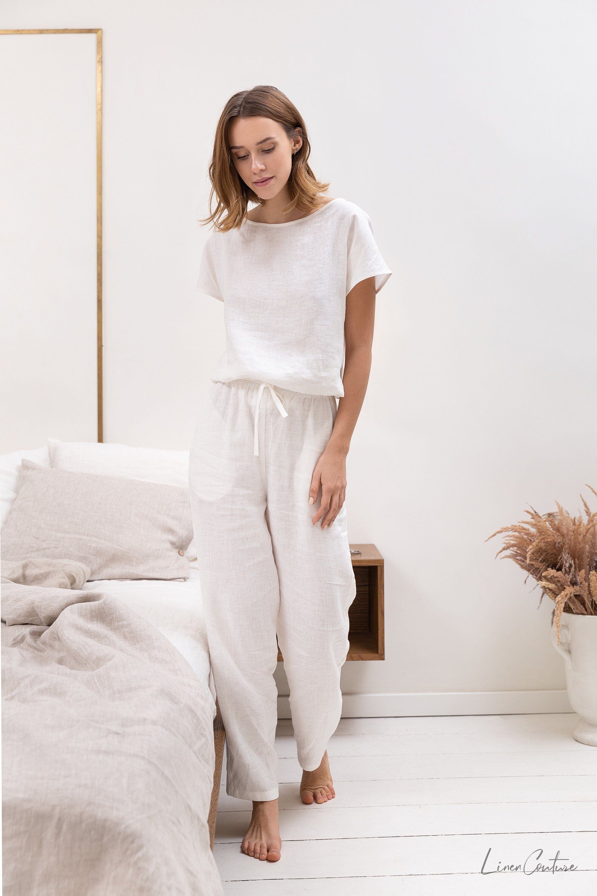 Elegant white linen pajama set featuring a boat neckline, short sleeves, and long pants with an adjustable waistband, perfect for lounging.
