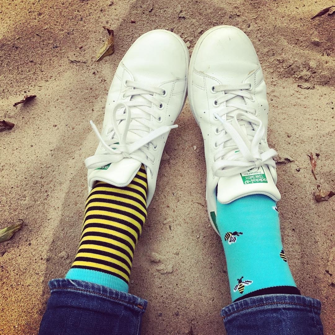 A pair of women's cotton socks featuring one striped sock and one with bees, in vibrant blue and yellow colors.