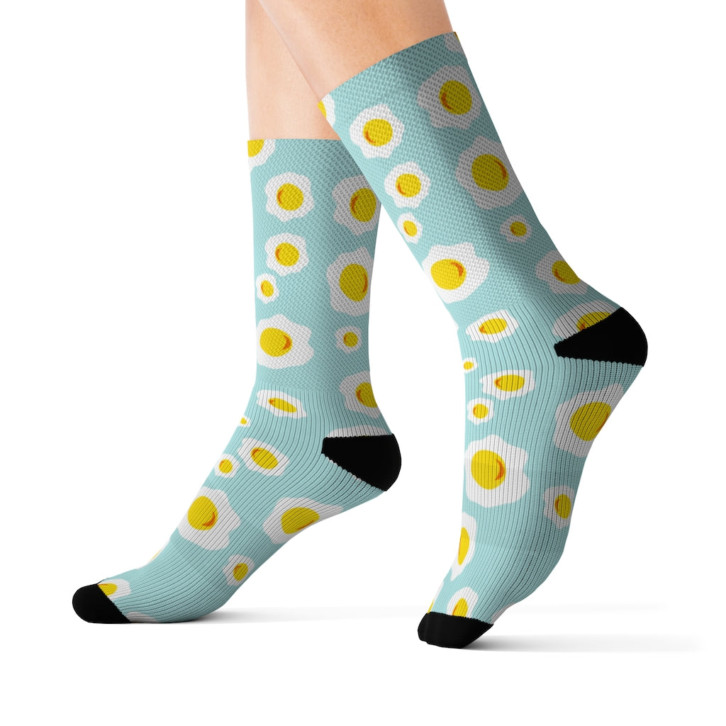 A pair of colorful novelty socks featuring a sunny side up eggs print, showcasing their vibrant design and comfortable ribbed tube.
