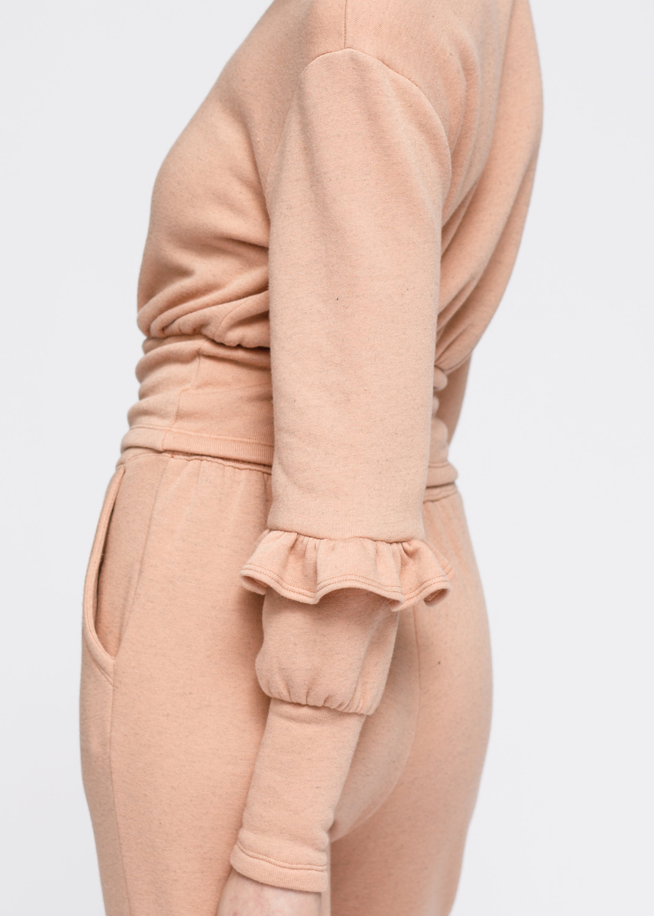 Peach crewneck sweatshirt with ruffle sleeve and elasticized waist, showcasing a stylish and comfortable design.