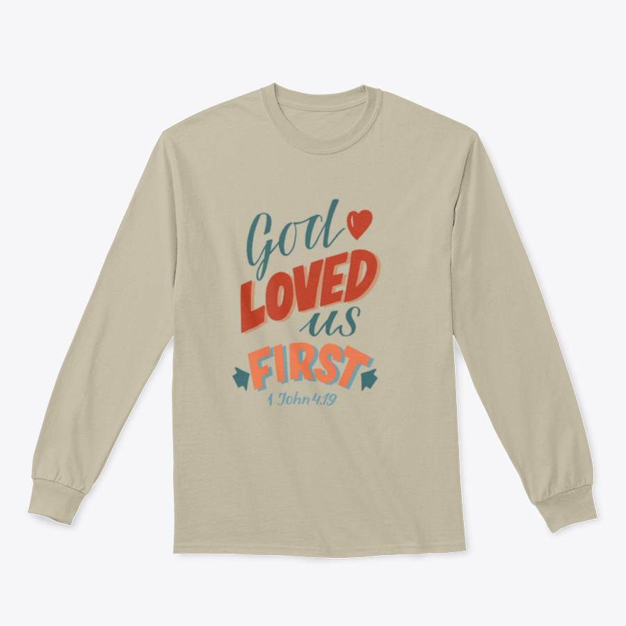 A modern t-shirt featuring the motivational quote 'God Loved Us First', made from soft cotton fabric, displayed on a neutral background.