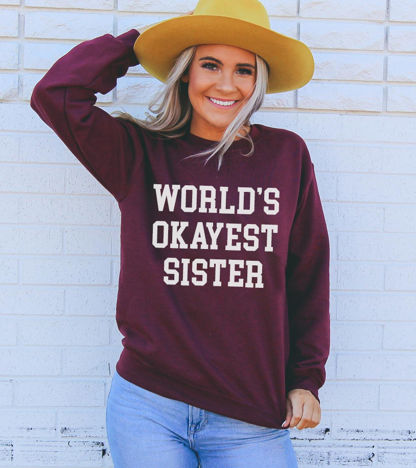 A cozy unisex sweatshirt featuring the phrase 'World's Okayest Sister' in a fun font, perfect for casual wear.