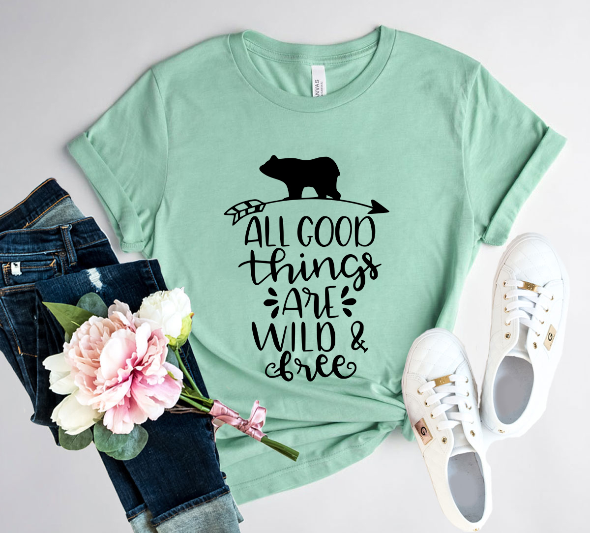 A unisex T-shirt featuring the phrase 'All Good Things Are Wild And Free' printed in a stylish font, made from soft ring spun cotton, available in various colors.