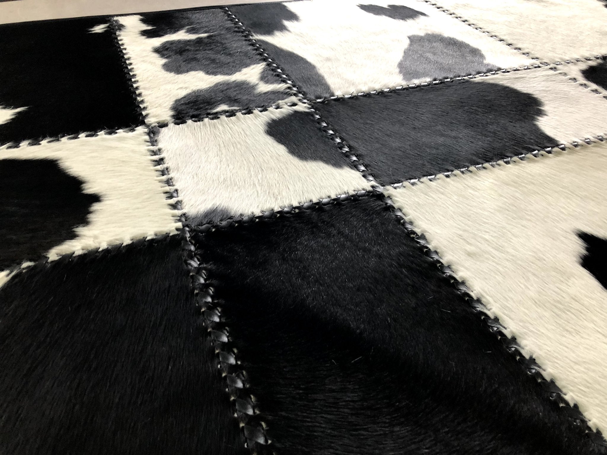 Handmade black and white patchwork cow skin rug, showcasing a luxurious design with natural leather texture.