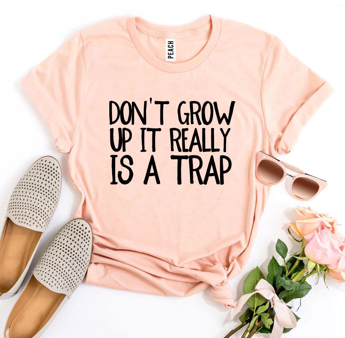 A stylish black t-shirt featuring the phrase 'Don’t Grow Up It Really Is a Trap' in bold white letters, made from premium ring spun cotton.