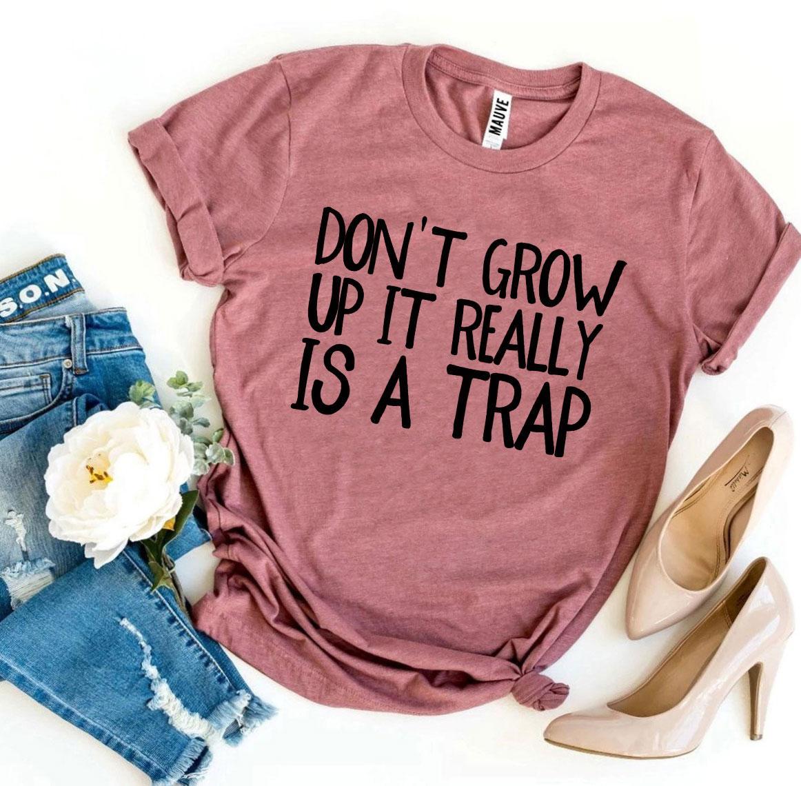 A stylish black t-shirt featuring the phrase 'Don’t Grow Up It Really Is a Trap' in bold white letters, made from premium ring spun cotton.