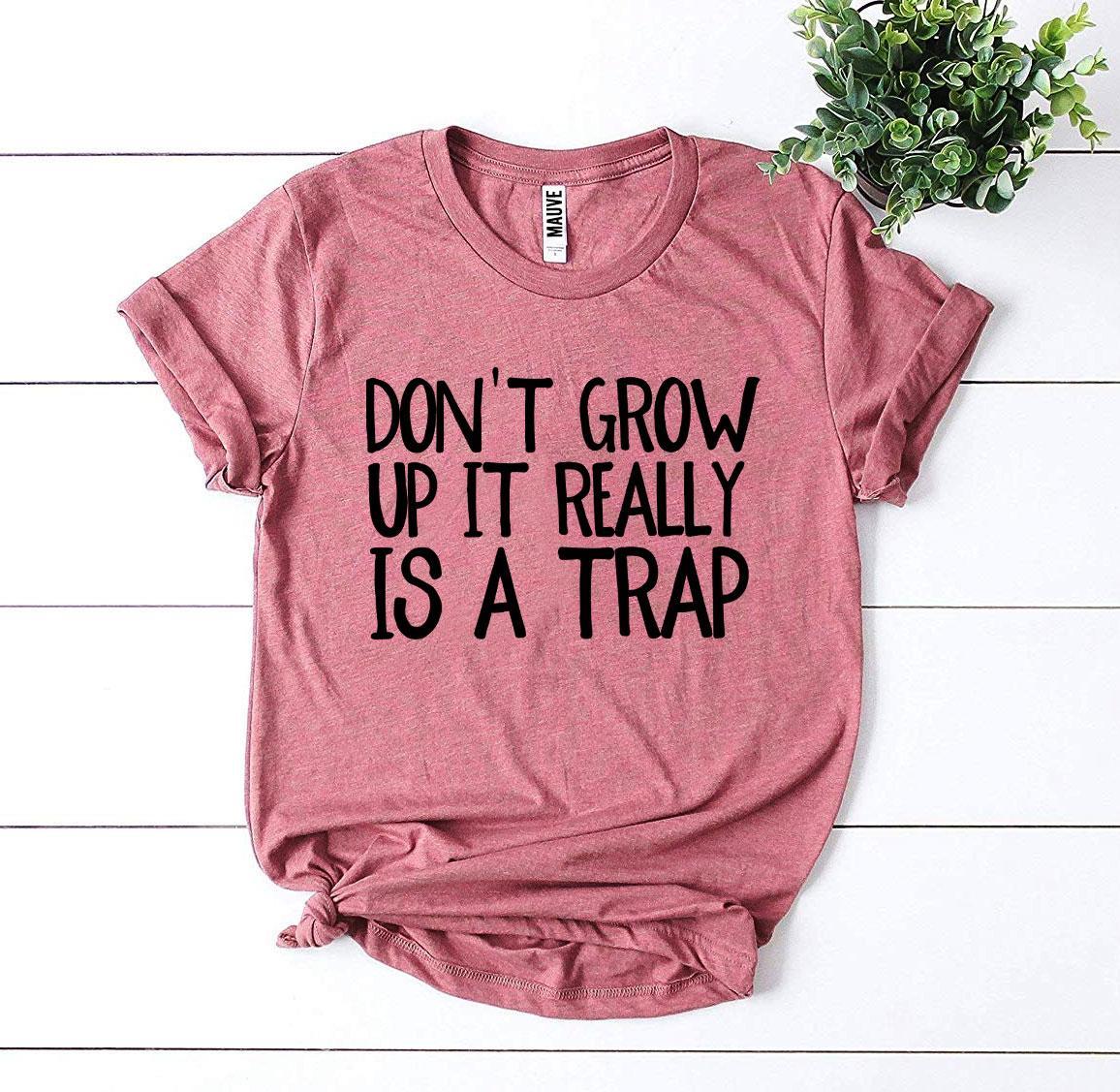 A stylish black t-shirt featuring the phrase 'Don’t Grow Up It Really Is a Trap' in bold white letters, made from premium ring spun cotton.