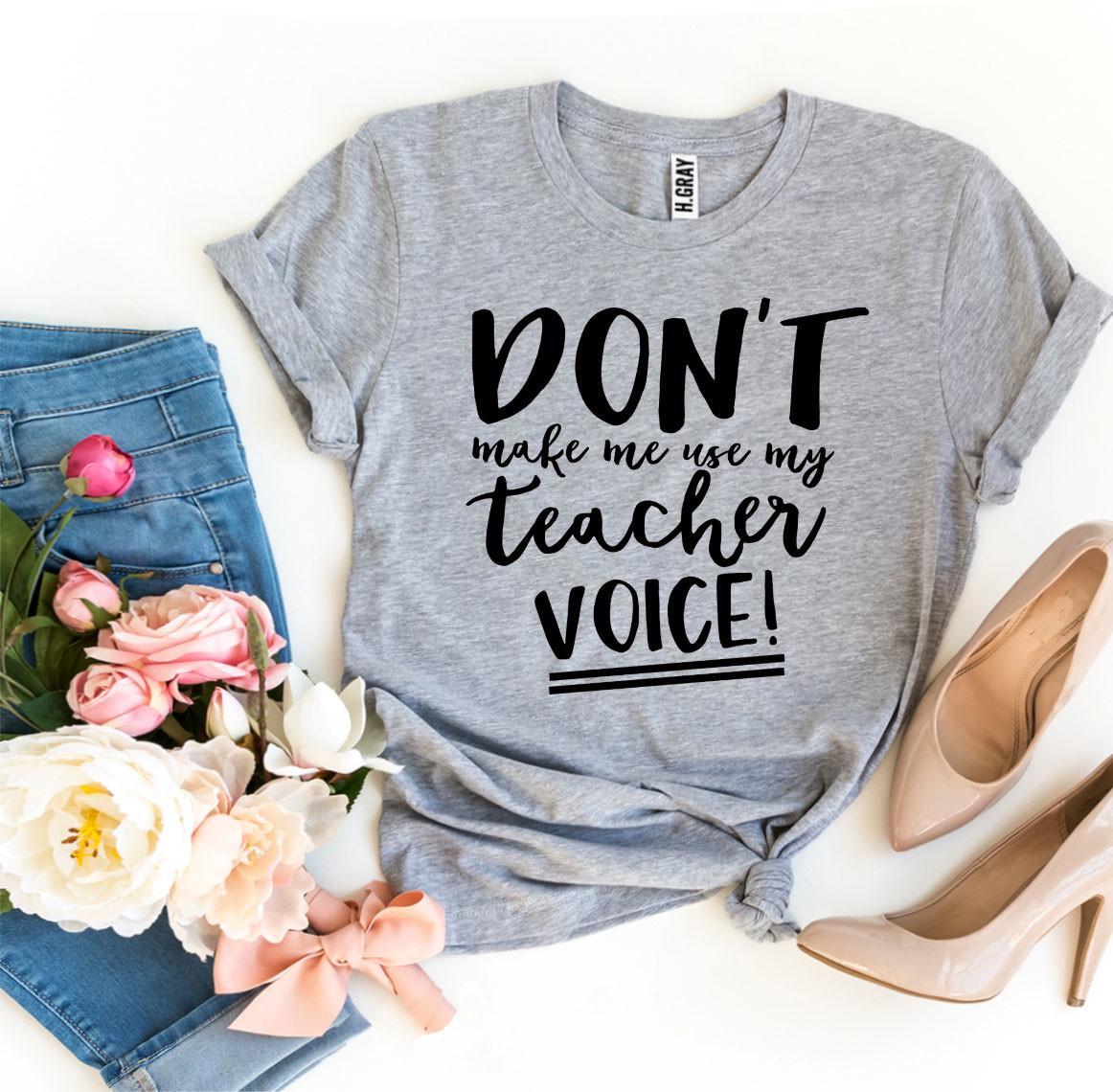 A black t-shirt featuring the phrase 'Don’t Make Me Use My Teacher Voice!' in bold white letters, made from soft ring spun cotton.
