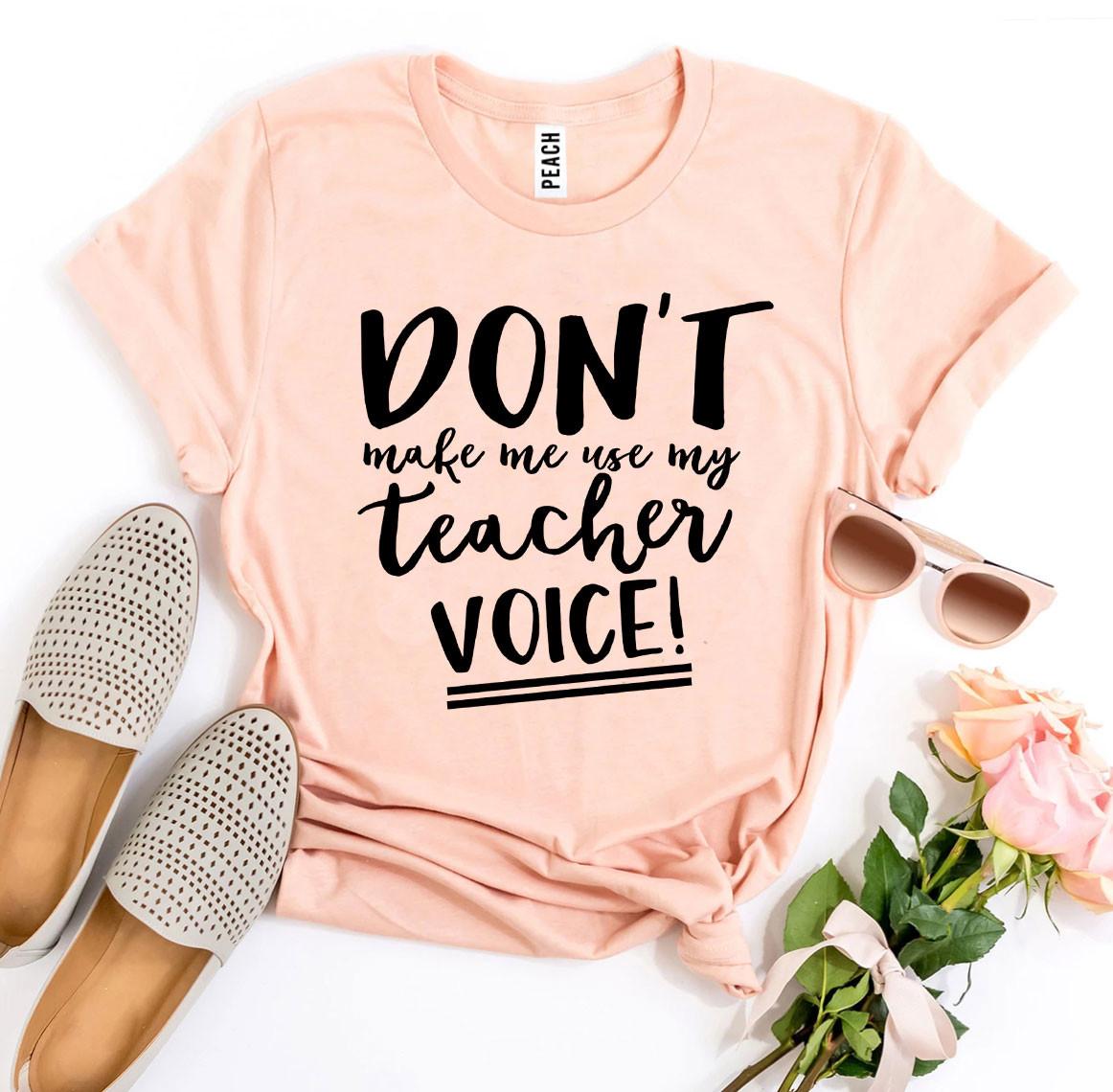 A black t-shirt featuring the phrase 'Don’t Make Me Use My Teacher Voice!' in bold white letters, made from soft ring spun cotton.