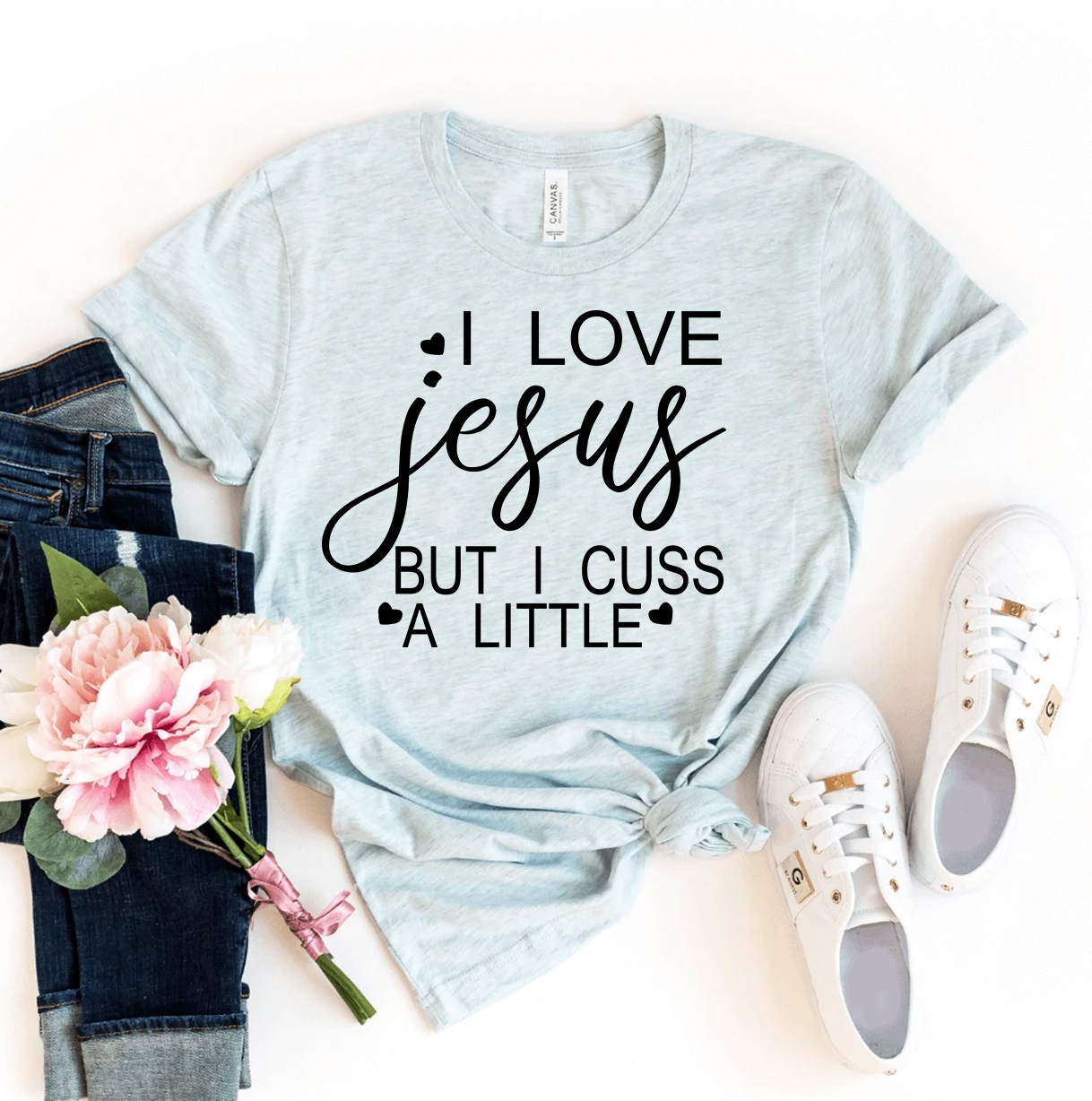 I Love Jesus But I Cuss A Little T-shirt in various sizes, showcasing its soft fabric and humorous design.