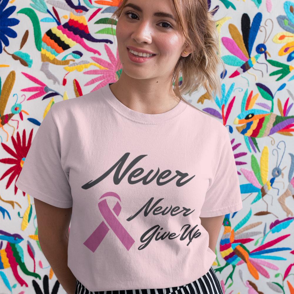 A soft pink t-shirt featuring the phrase 'Never Never Give Up' with a pink ribbon, symbolizing breast cancer awareness.