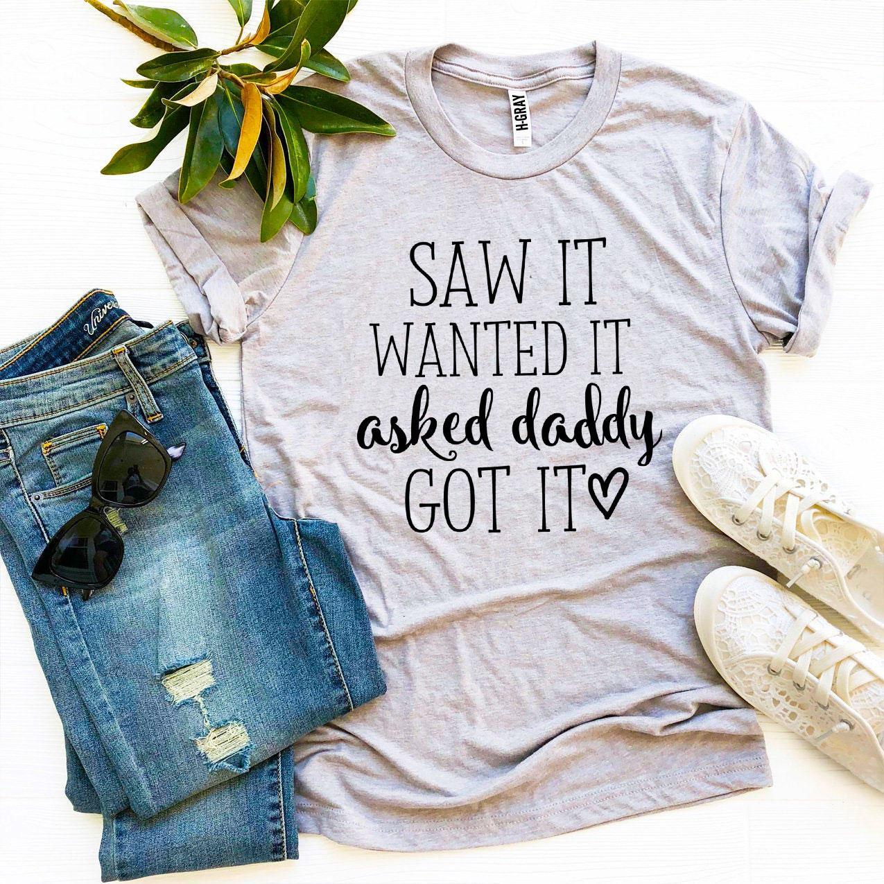 A stylish black t-shirt featuring the phrase 'Saw It Wanted It Asked Daddy Got It' printed in vibrant colors, made from soft ring spun cotton.