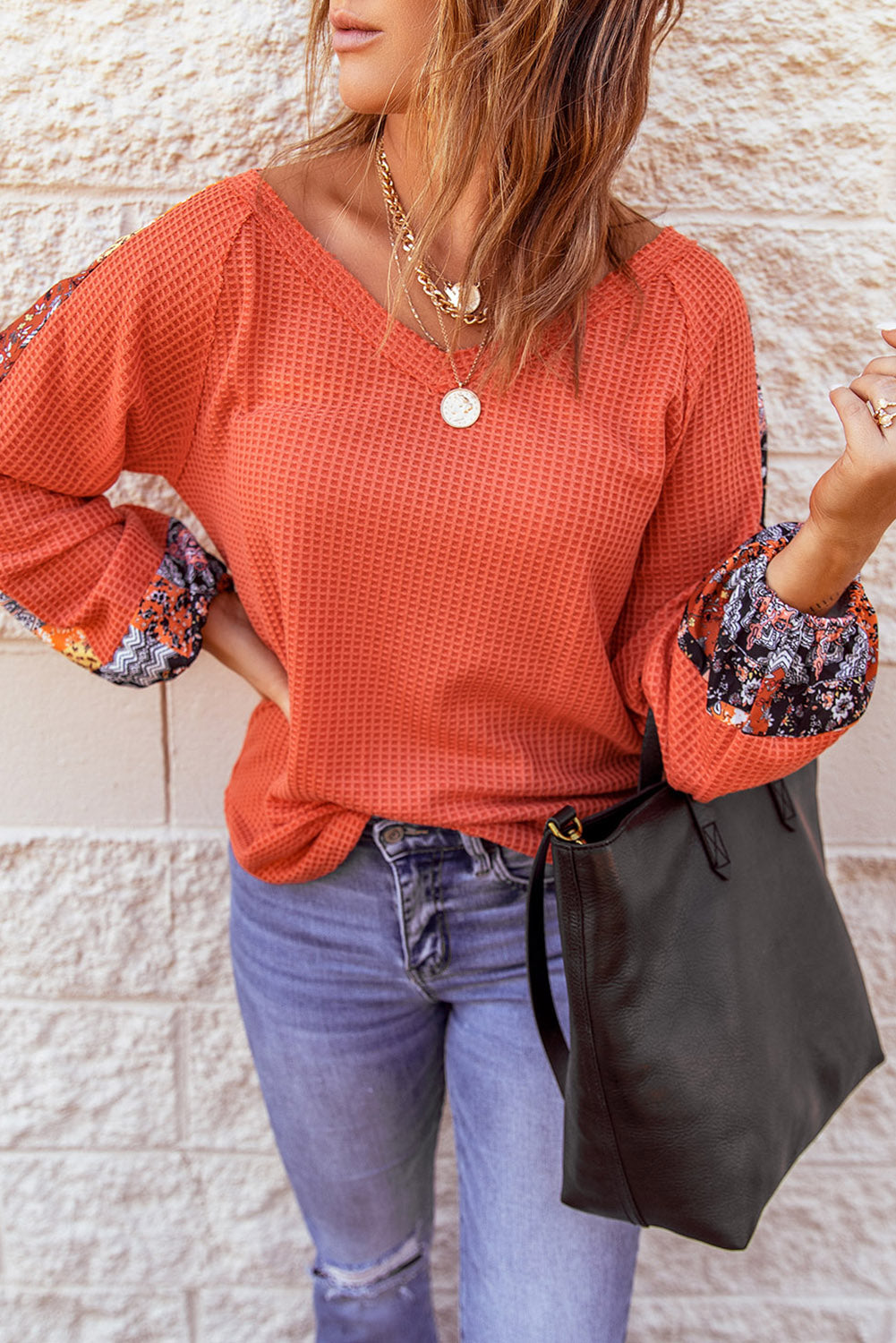 Orange long sleeve thermal knit top with floral print patchwork lantern sleeves and v-neckline, showcasing a stylish and comfortable design.