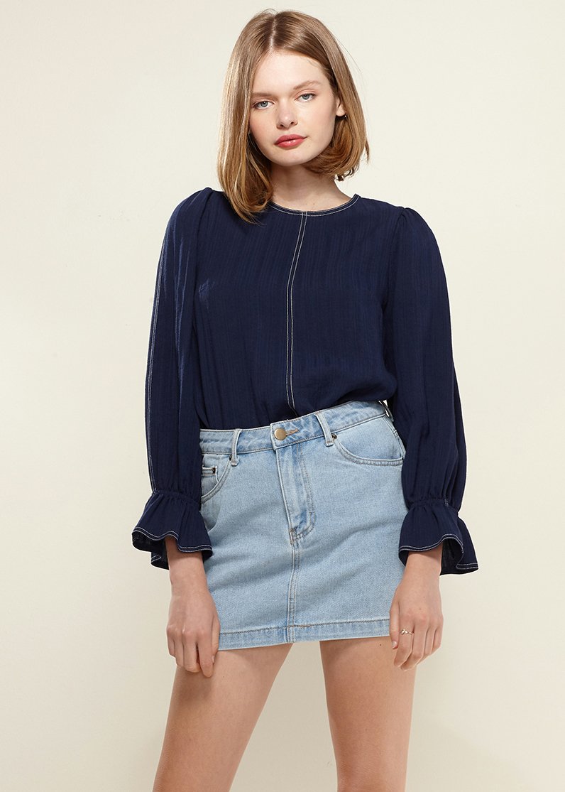 Women's navy top featuring stitch accents, puff shoulders, and bell cuffs, perfect for versatile styling.