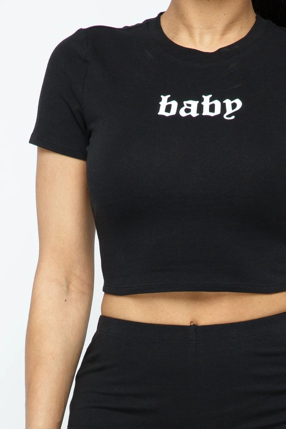 A stylish woman wearing a 2-piece short sleeve outfit set, featuring a round neck crop top and matching shorts in a solid color, perfect for active wear.