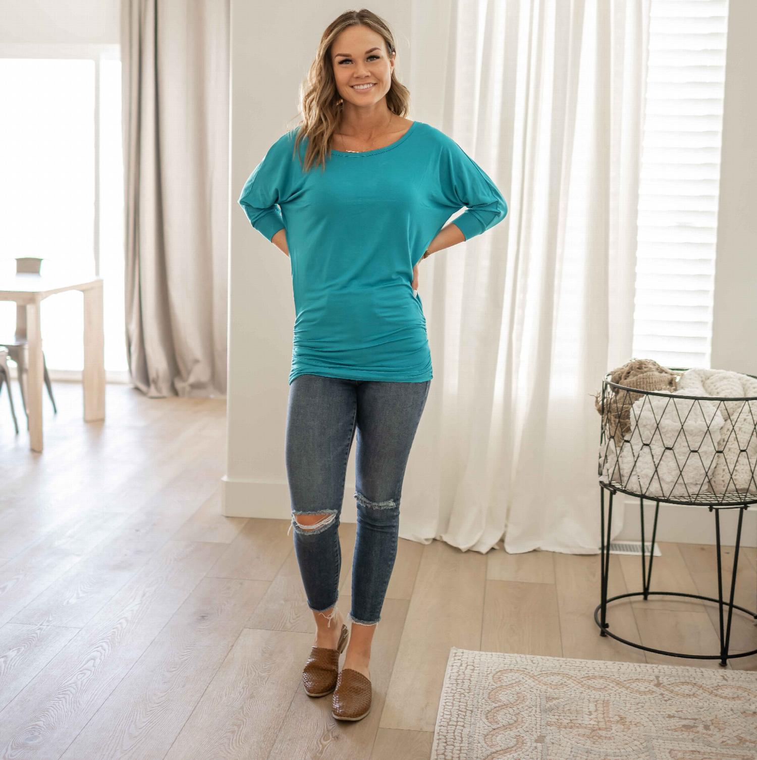 A stylish 3/4 sleeve blouse with side shirring, featuring a relaxed fit and wide boatneck collar, available in various colors.