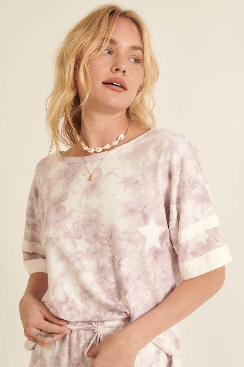 A lavender star-pattern tie-dye knit top with short sleeves and varsity stripe trim, showcasing a relaxed oversized fit.