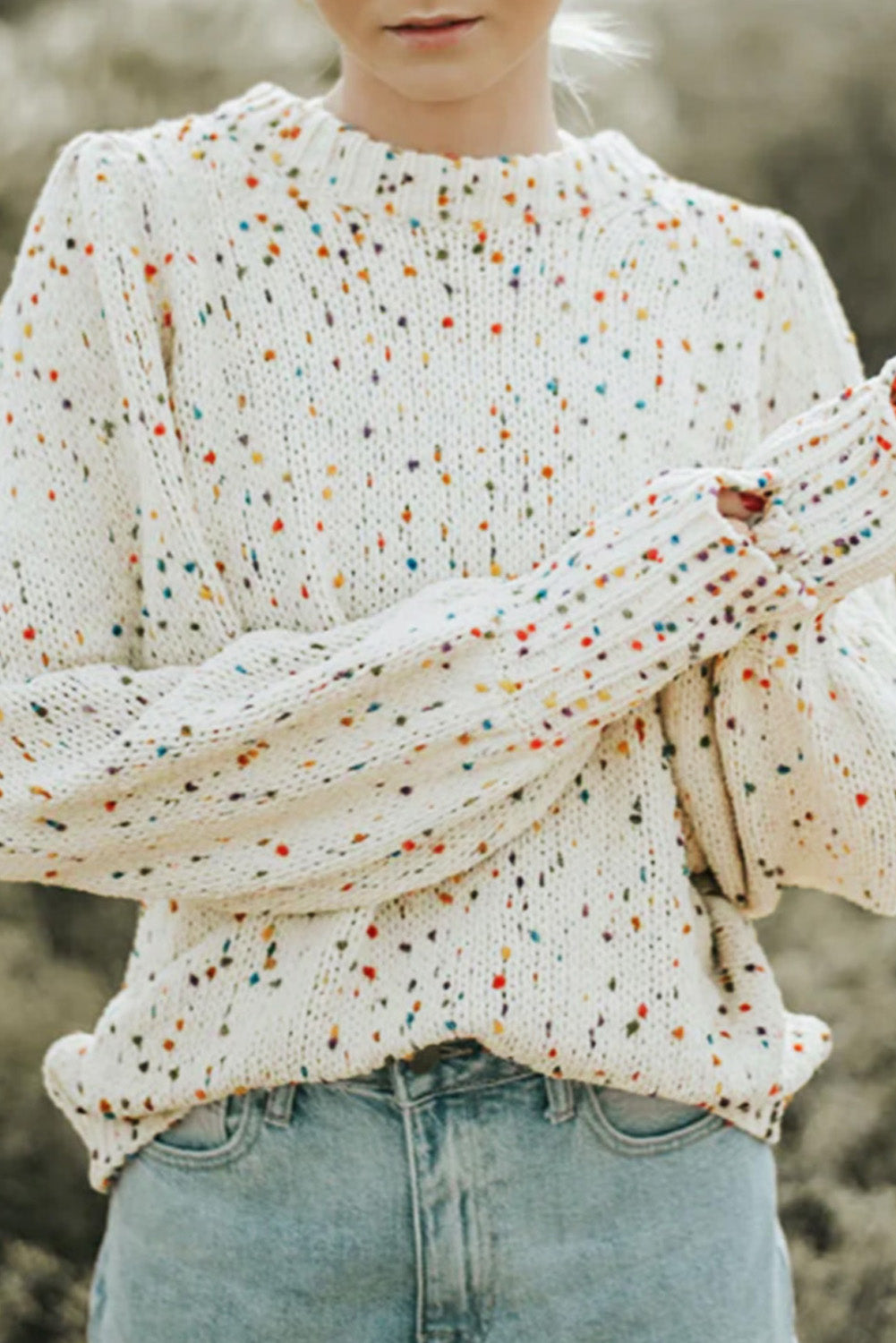 Beige crew neck sweater with colorful dots, showcasing cable knit texture and long sleeves.