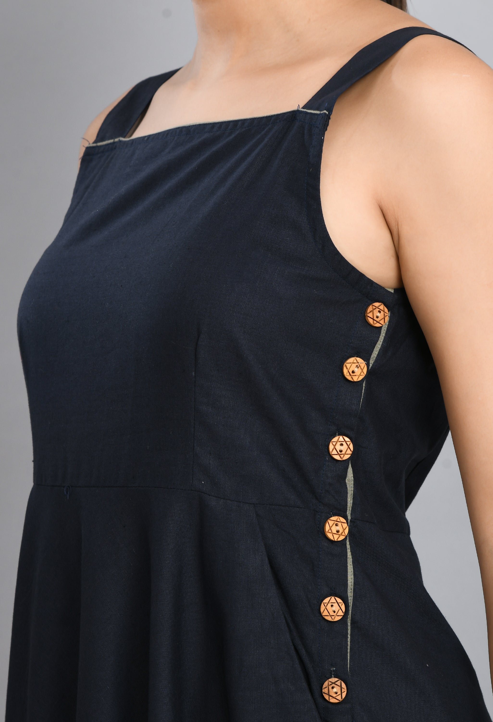 A stylish blue linen sleeveless dress with wood buttons and an asymmetrical hem, perfect for casual wear.