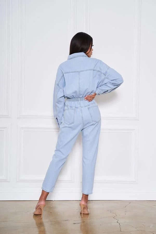 Light blue denim jumpsuit with button front and pockets, featuring long sleeves and a stylish design.