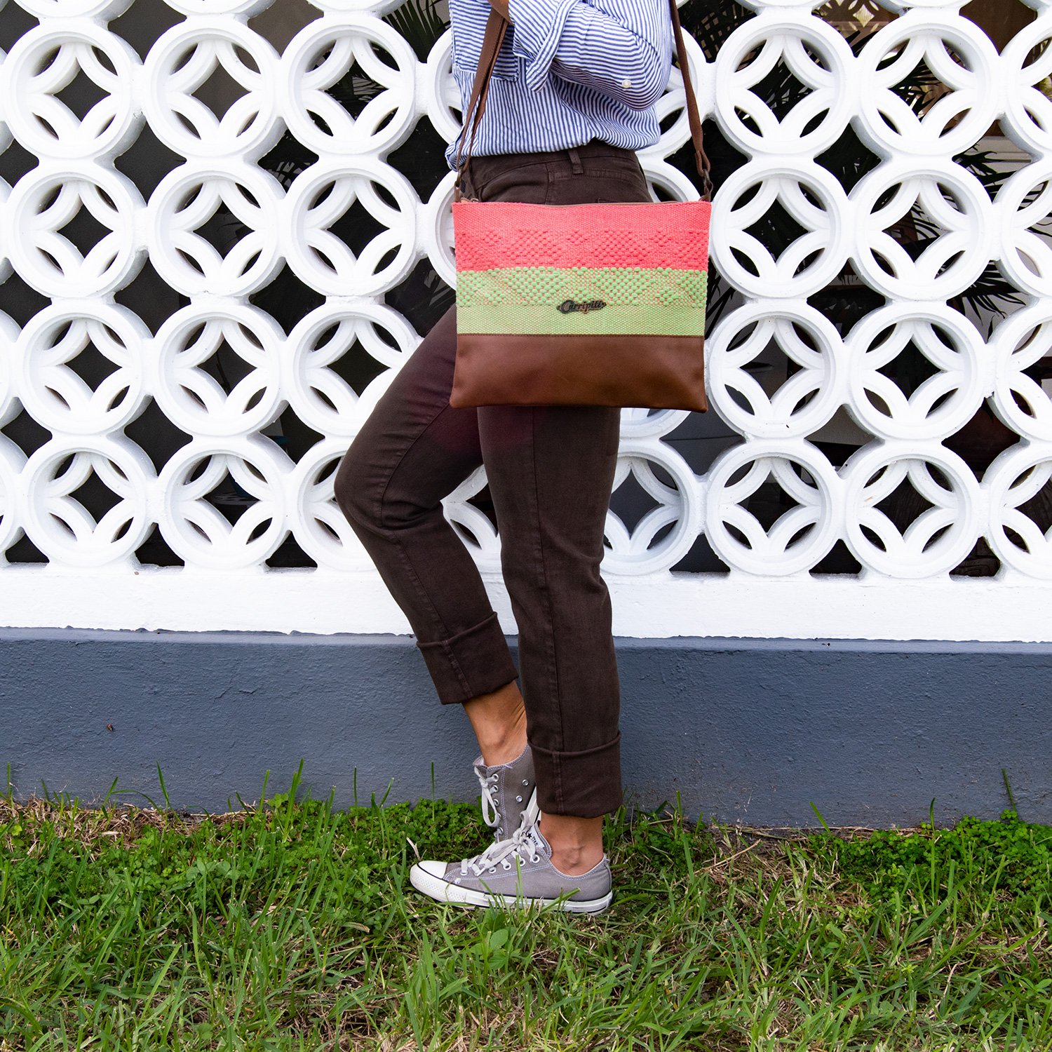 Brown leather cross-body bag featuring coral and green woven stripe, showcasing ethnic motifs and adjustable strap.