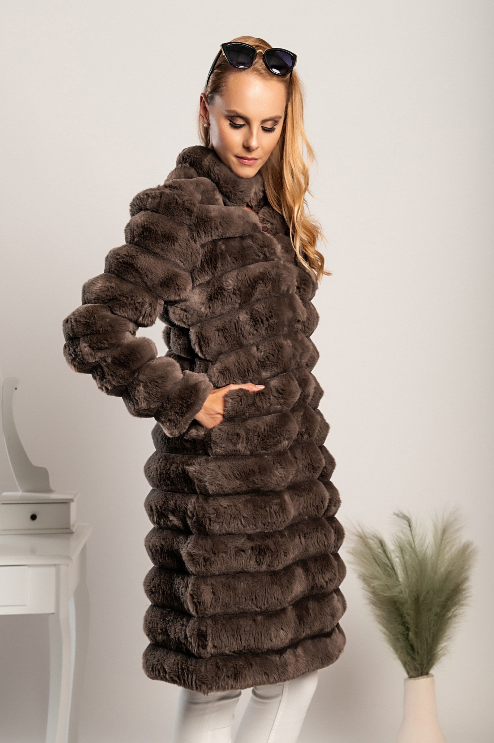 Daljši eleganten plašč iz umetnega krzna Benimia v rjavi barvi, z visokim ovratnikom in dvema žepoma.