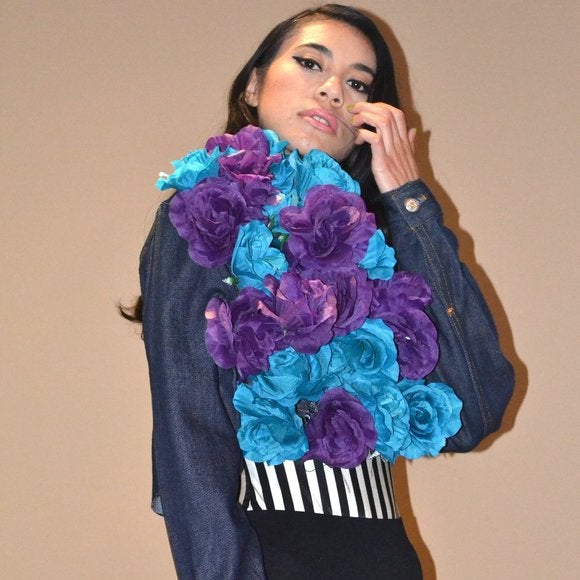 A stylish dark blue denim cropped jacket featuring embroidered roses on one side, showcasing a raw edge hemline.