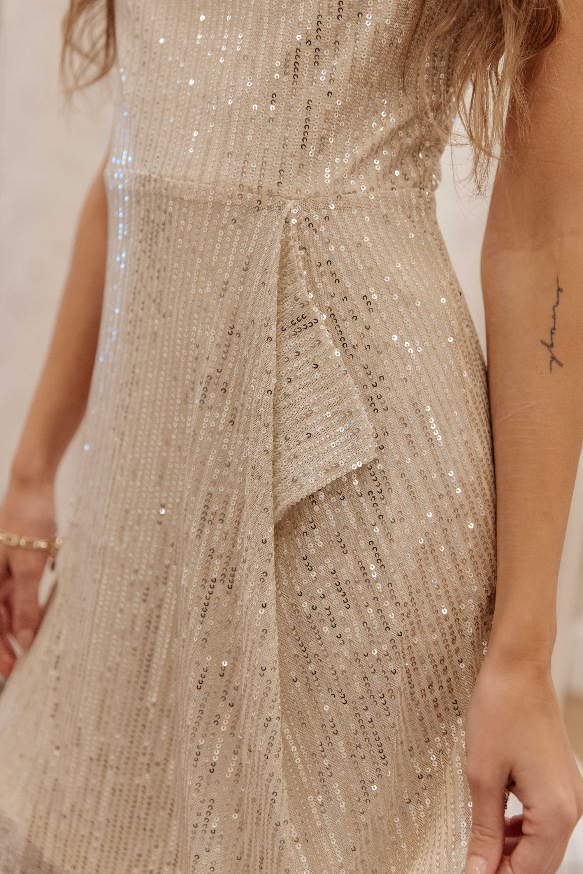 A glamorous gold sequined dress with ruffle detail at the waist, showcasing adjustable straps and a shimmering finish.