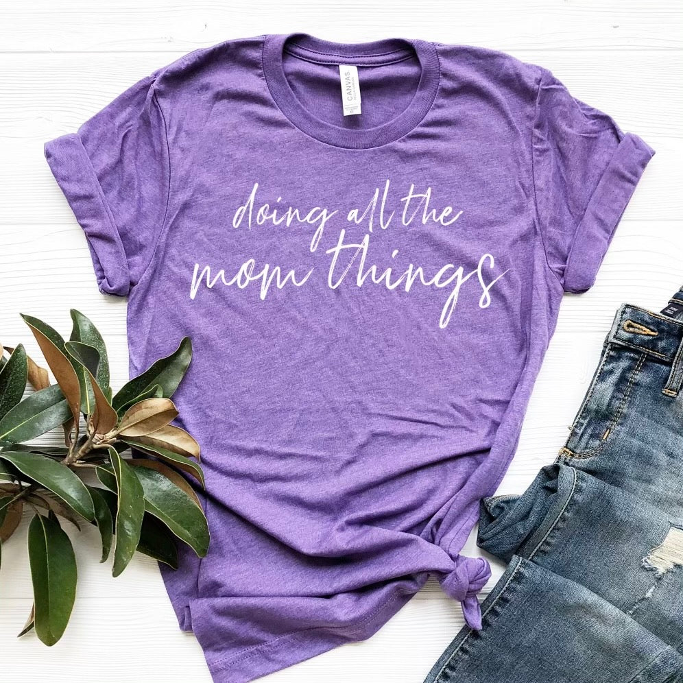 Heather team purple t-shirt with white ink design saying 'Doing All The Mom Things', showcasing a stylish and comfortable fit.