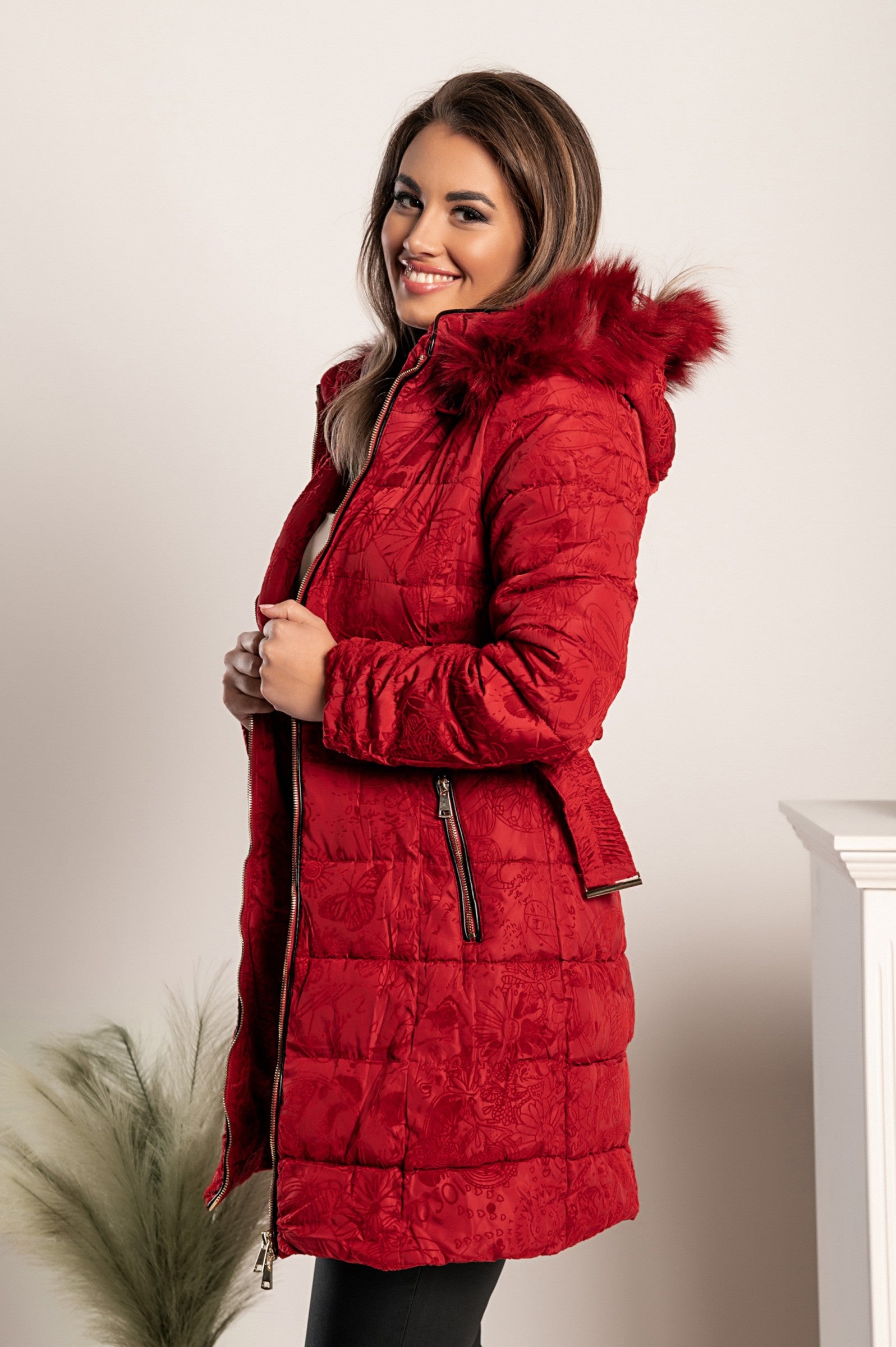 Dolga prešita bunda Remma v rdeči barvi z modrim vzorcem iz imitacije žameta, visokim ovratnikom in stranskima žepoma z zadrgo.