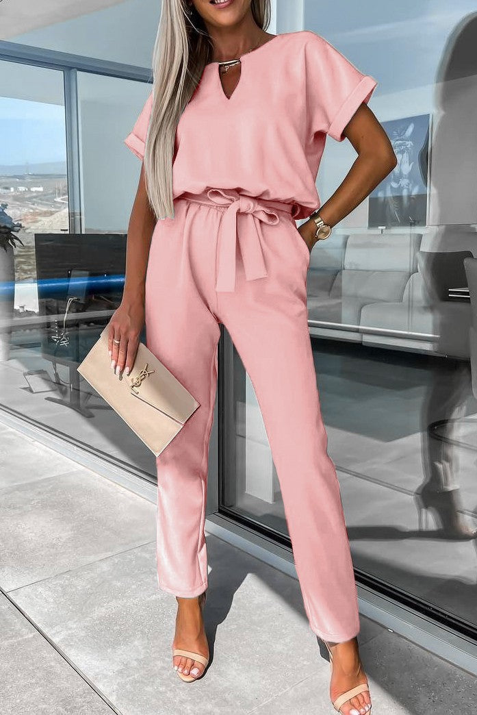 Elegant light pink jumpsuit featuring metallic detail, plunging neckline, and short sleeves, complete with a decorative belt.