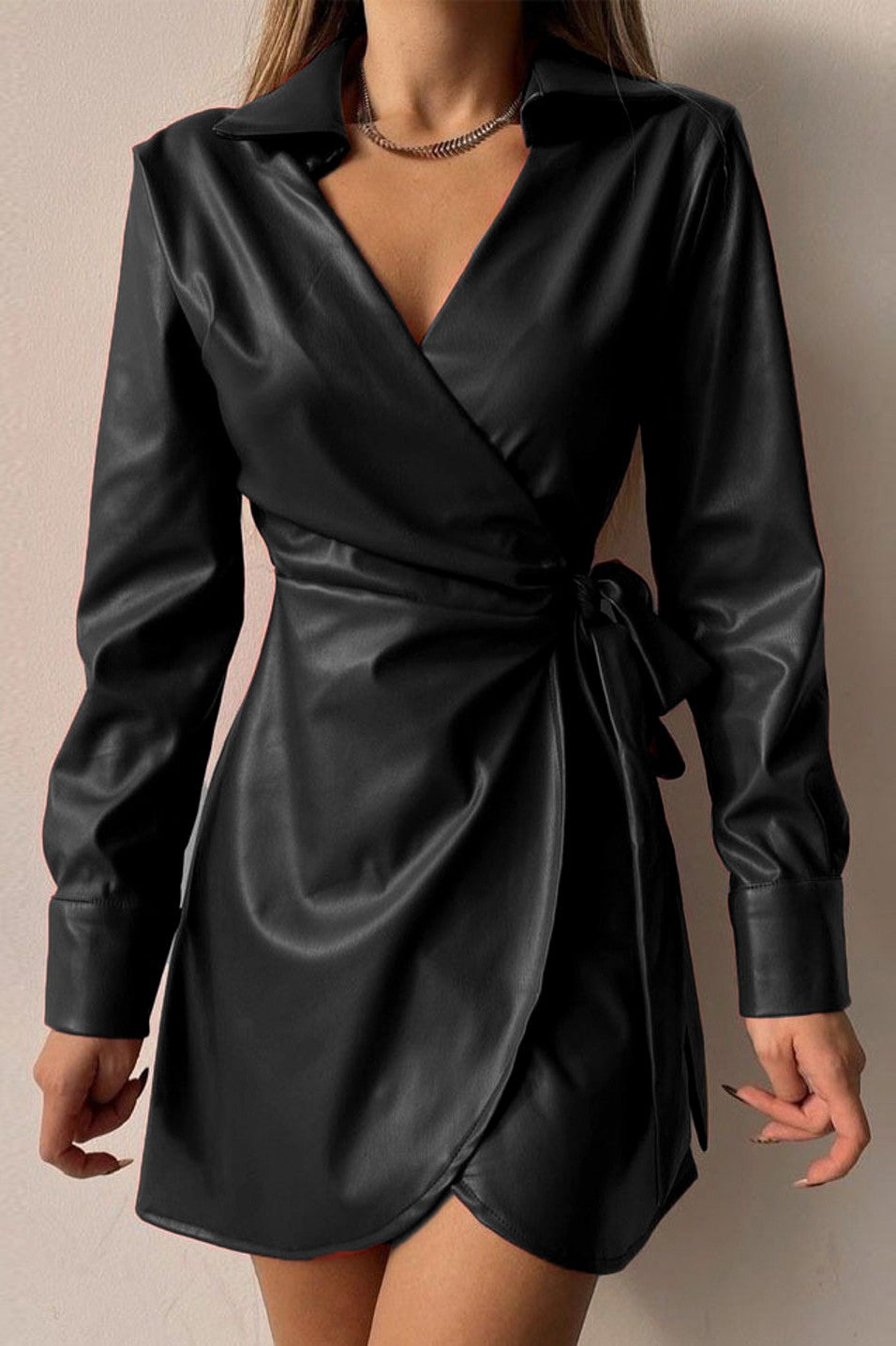 Elegant black mini dress made of faux leather with a folding collar and long sleeves, featuring a tied waist and knee-length skirt.