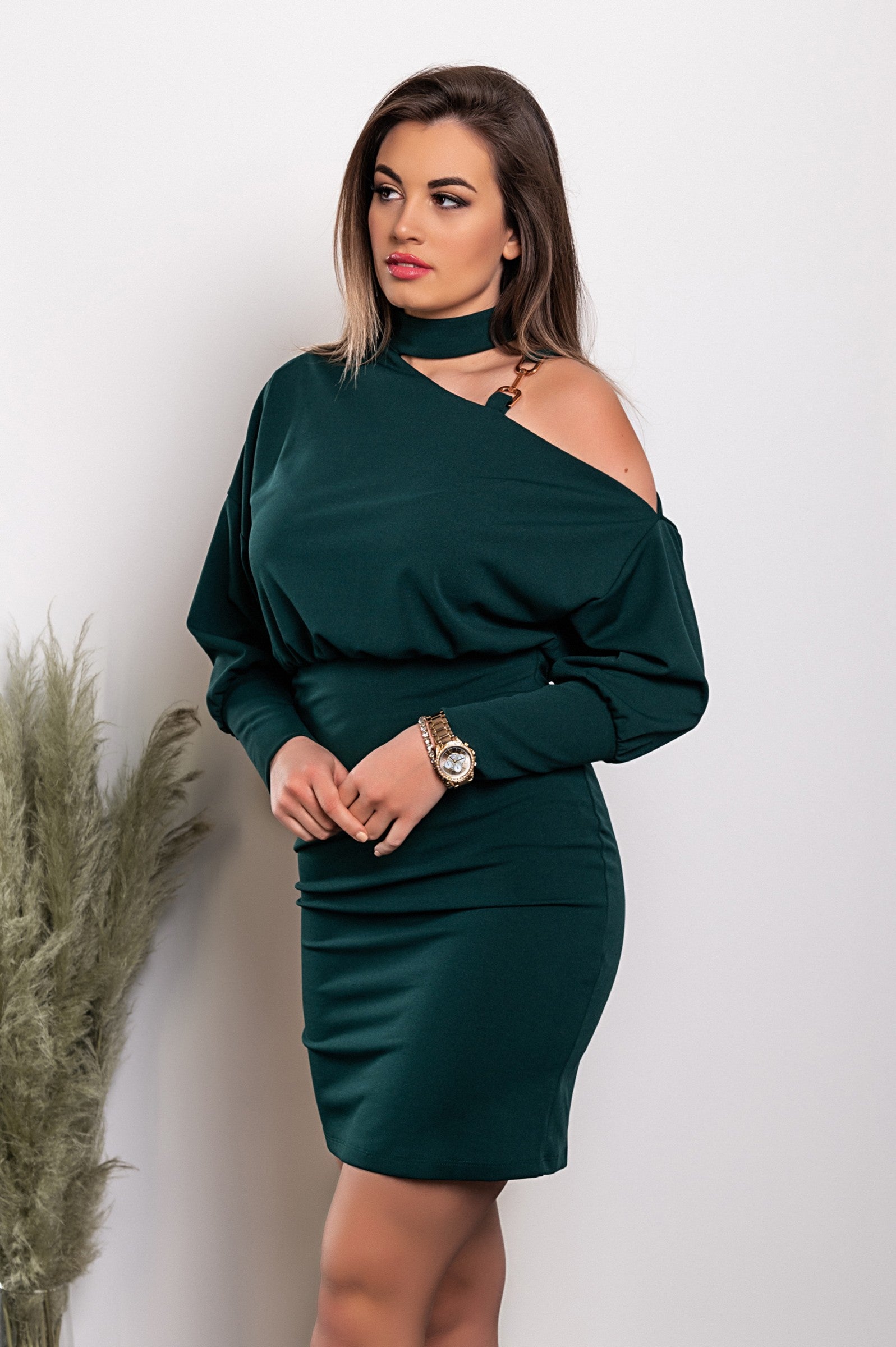 Elegant green mini dress with asymmetrical neckline and decorative chain, featuring a loose-fitting top and fitted mid-thigh skirt.