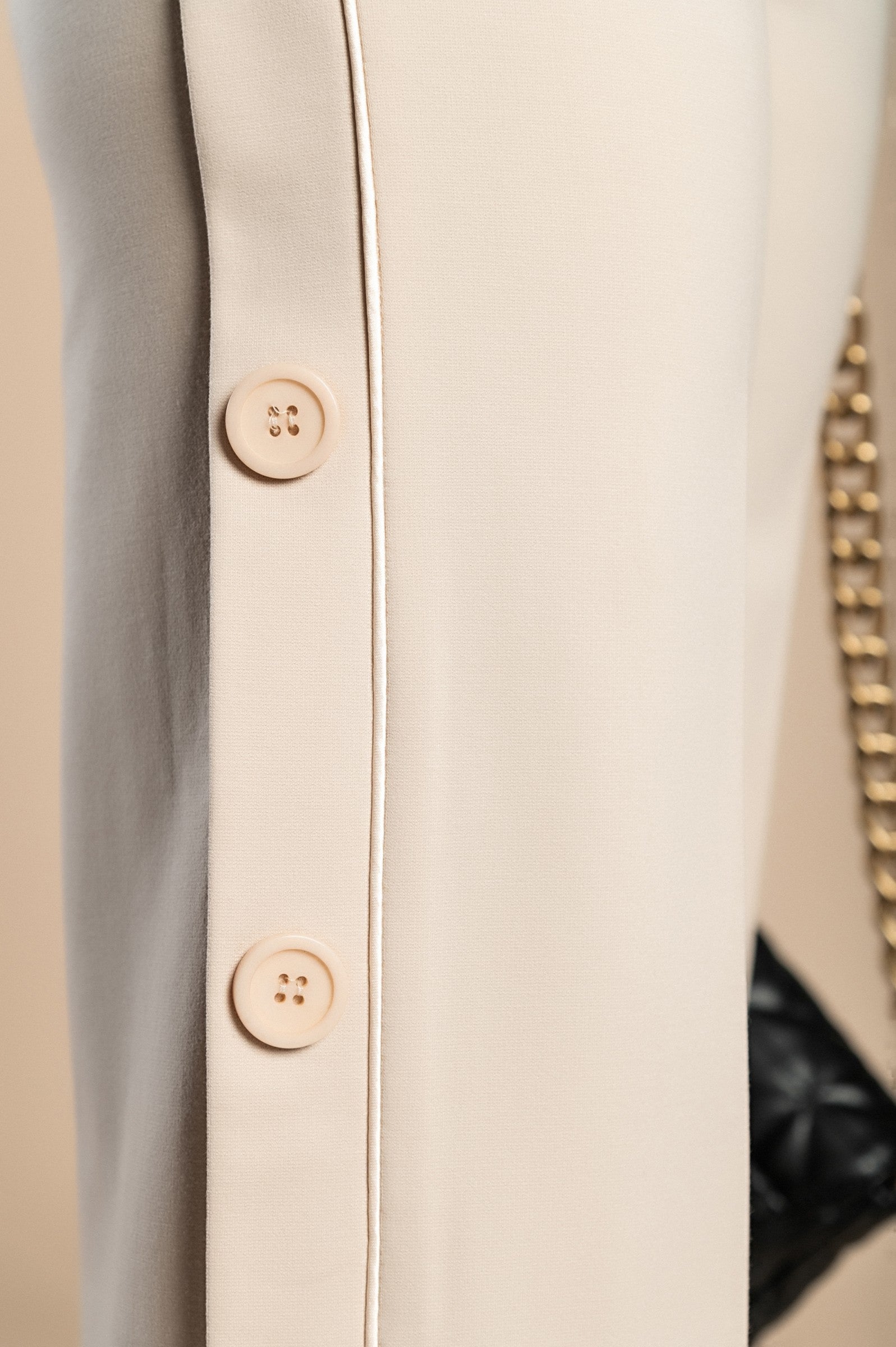 Elegant cream trousers with decorative buttons on the sides and an elasticated waist, showcasing a straight leg design.