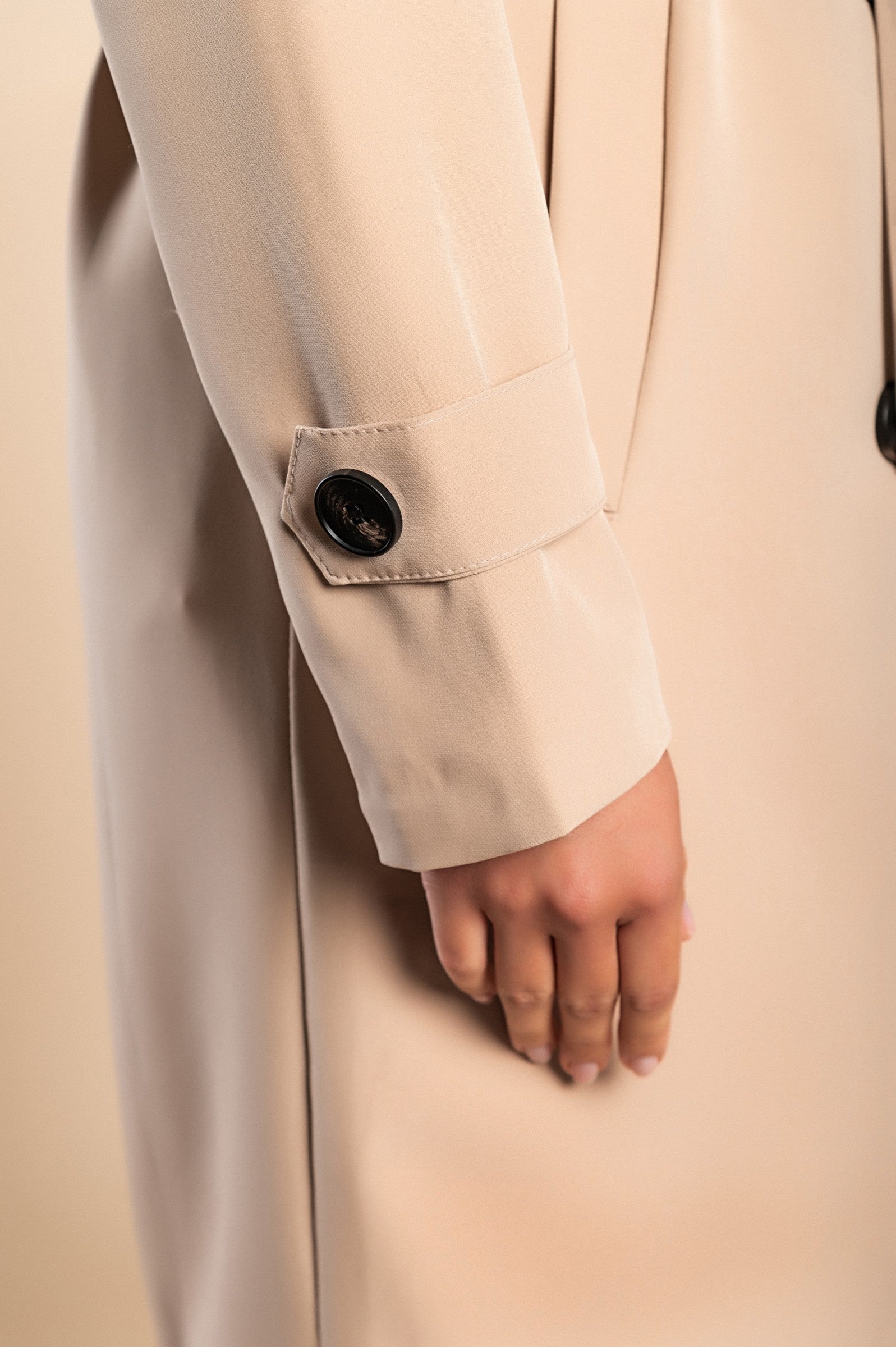 Eleganten bež trenčkot z gumbi, klasičnim ovratnikom in stranskimi žepi, dolžina do kolen.