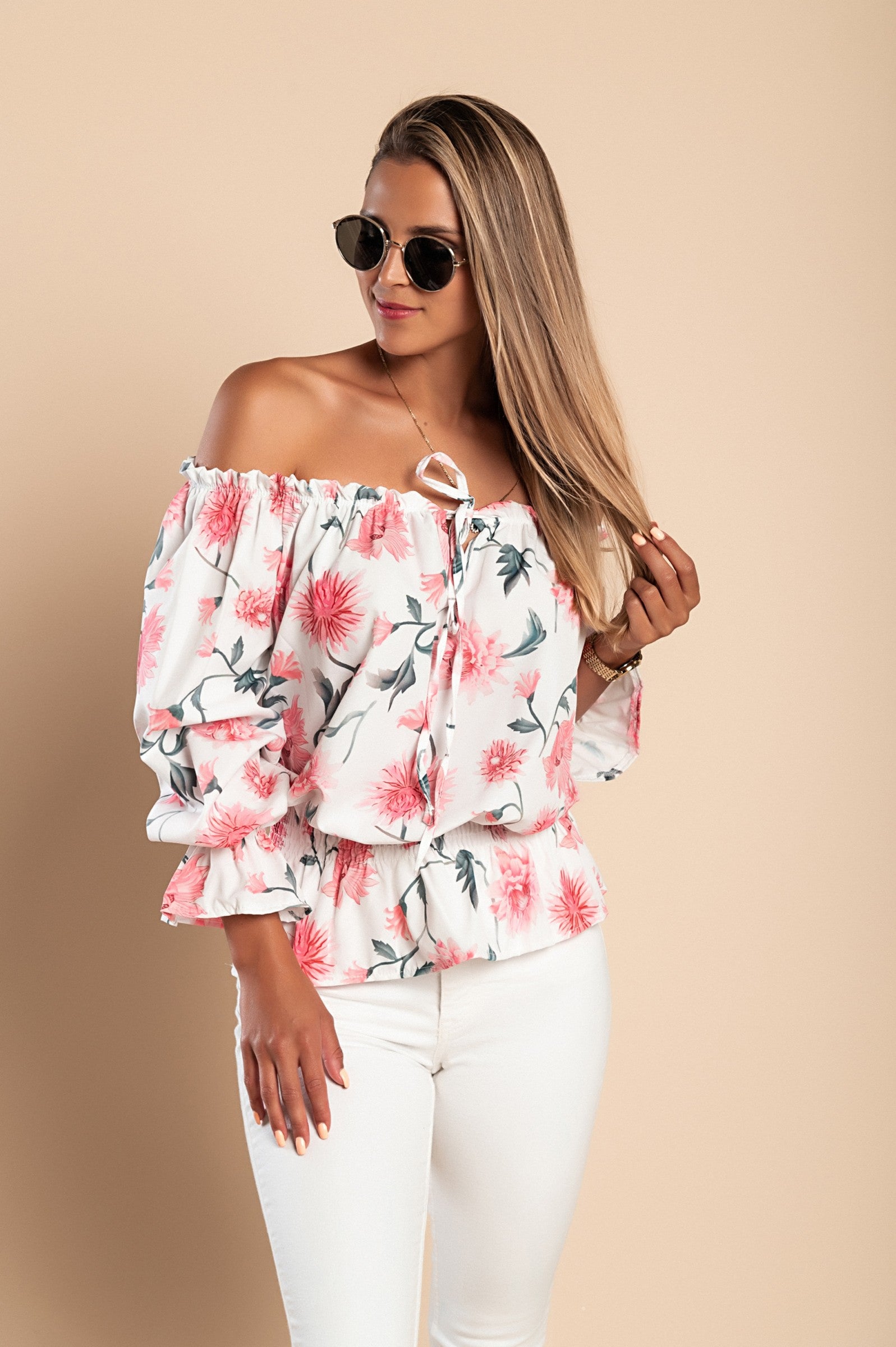 Elegantna bluza z odkritimi rameni, volančki in rožnatim potiskom, idealna za modno kombiniranje.