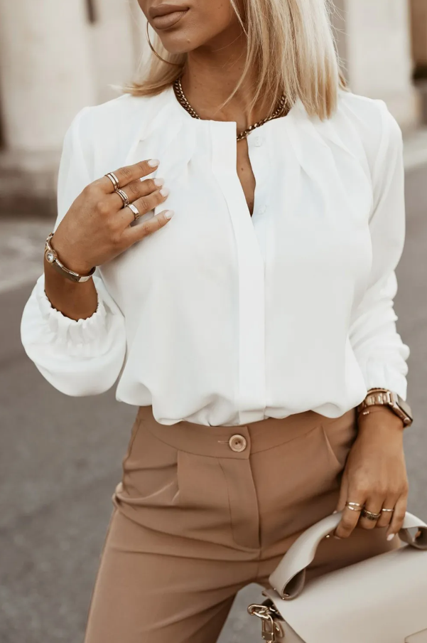 Elegantna bela srajca z okroglim ovratnikom in dolgimi rokavi, zaključena z elastiko.