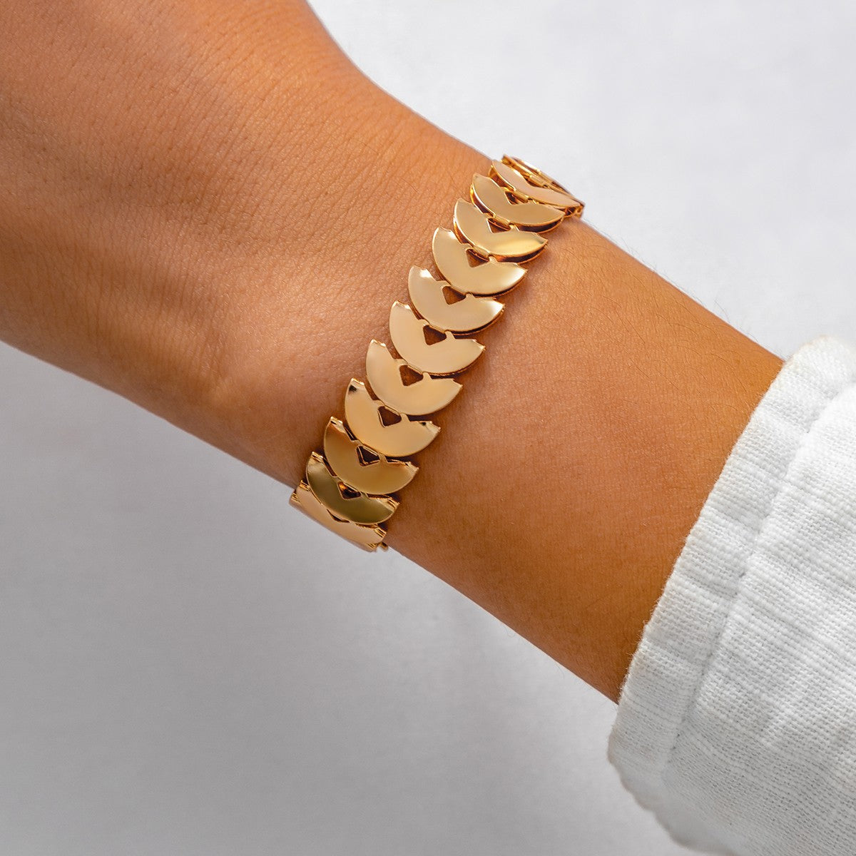 Elegantna zlatna zapestnica iz polkrožnih členov, ki se blešči v svetlobi.