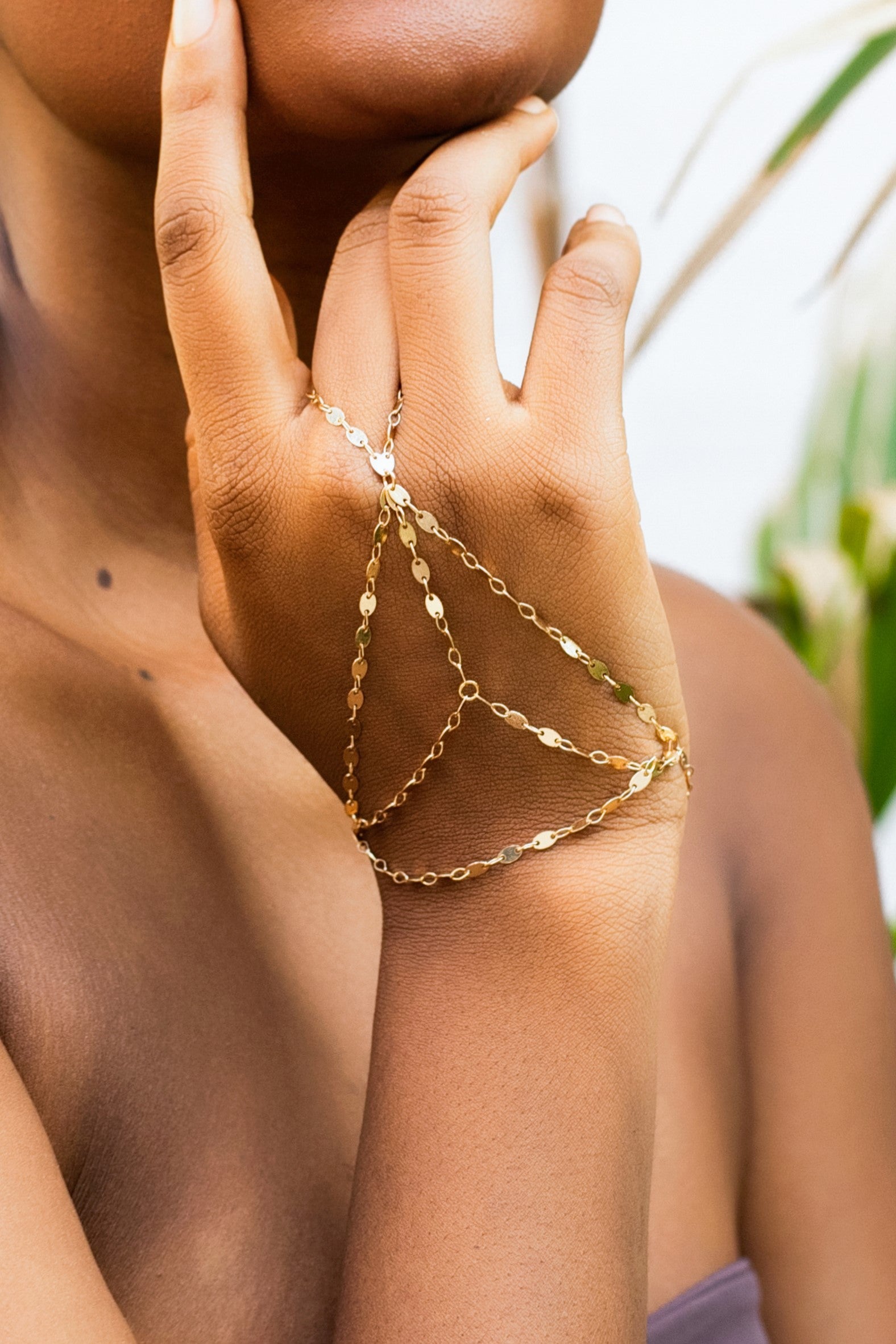 Elegantna zlatna zapestnica z okrasnimi detajli in verižico za okoli prsta, idealna za modno kombinacijo.