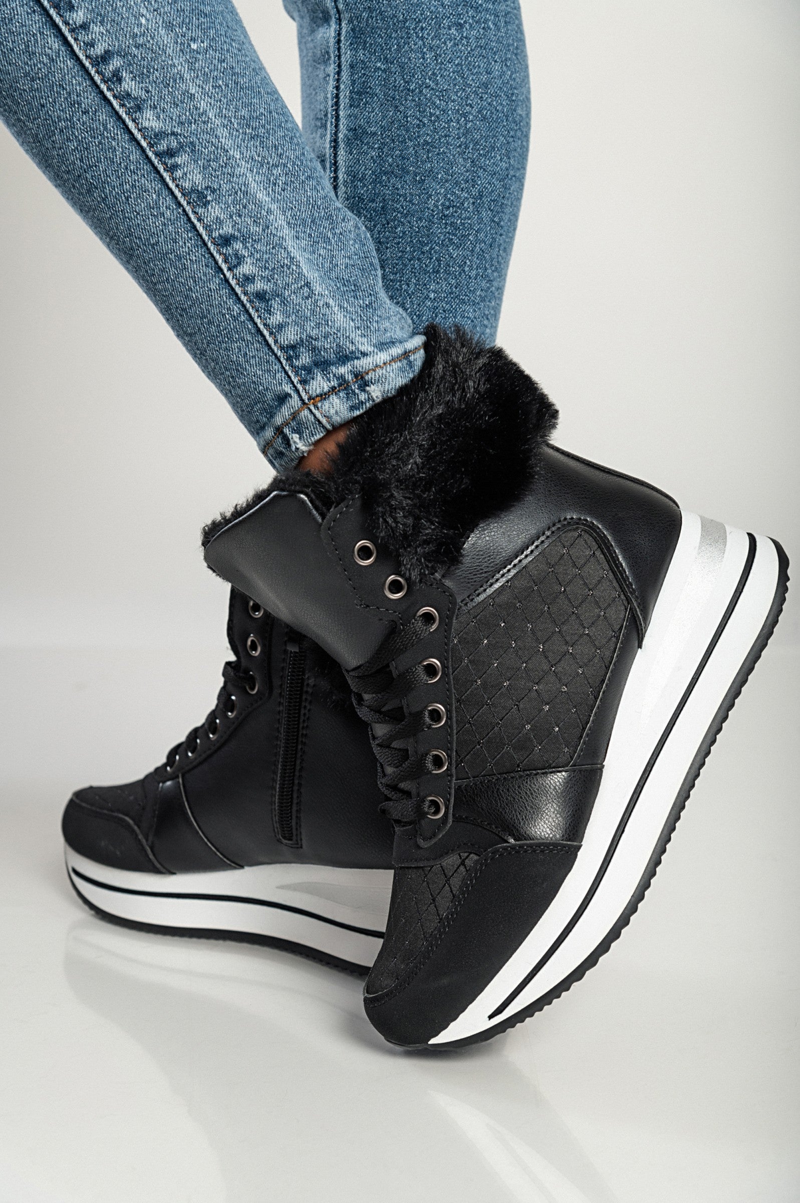 Black fashion sneakers made of faux leather and textile with raised sole and synthetic fur around the ankle.