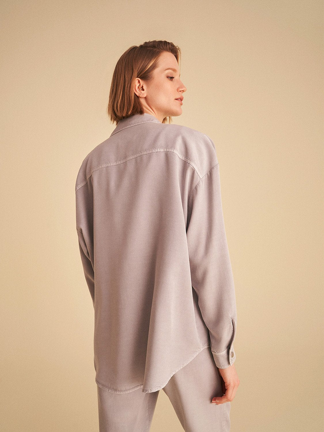 Flowy shirt with pockets, featuring long sleeves, snap buttons, and vibrant digital collage patterns in soft shades.