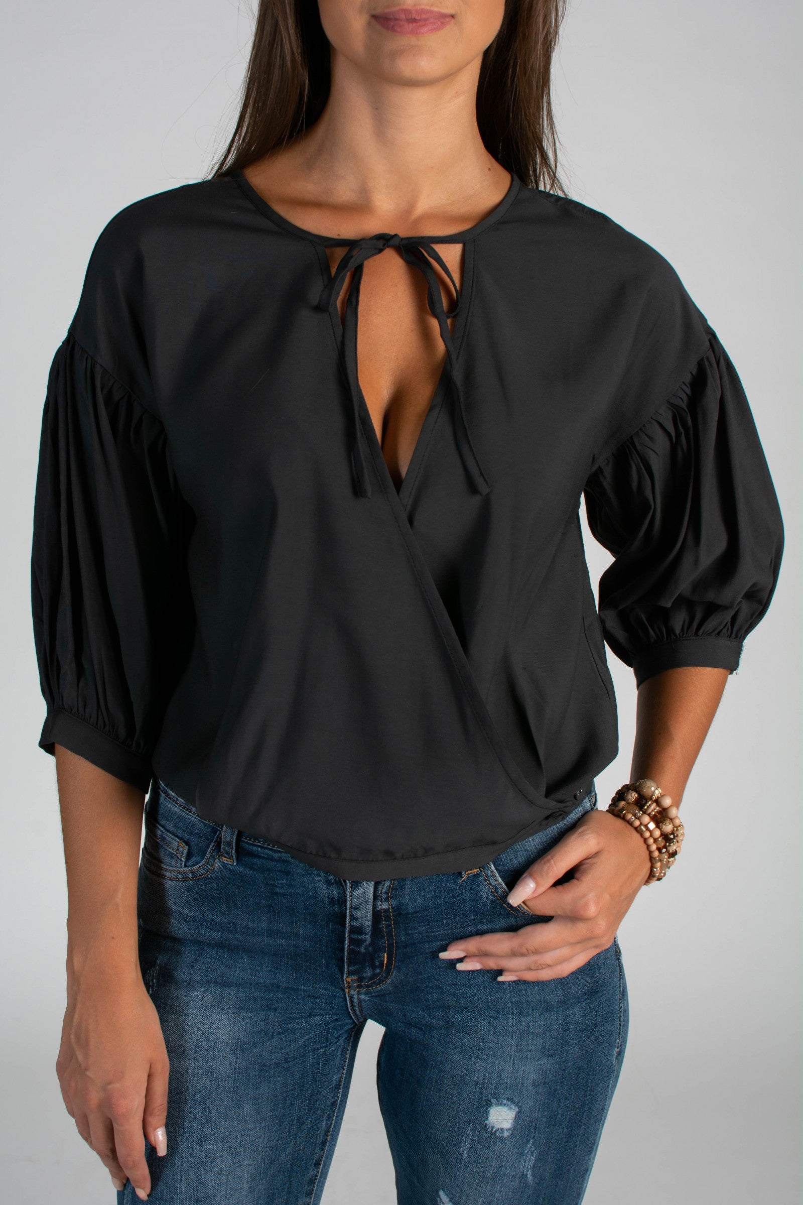 Elegant black folding blouse with short gathered sleeves and tie detail at décolleté.