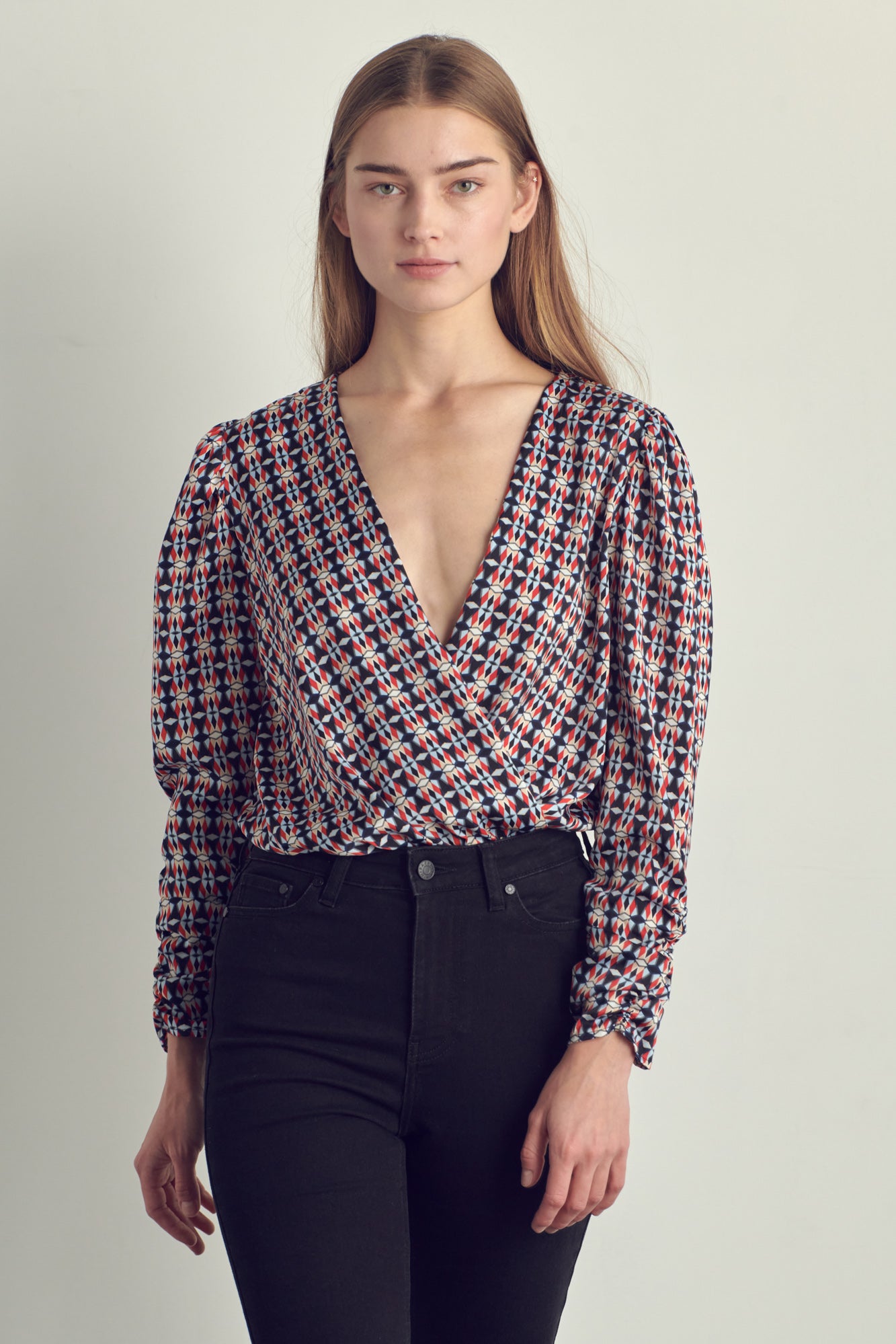 Ruched long sleeve surplice bodysuit in satin abstract print, featuring a stylish neckline and ruched cuffs.